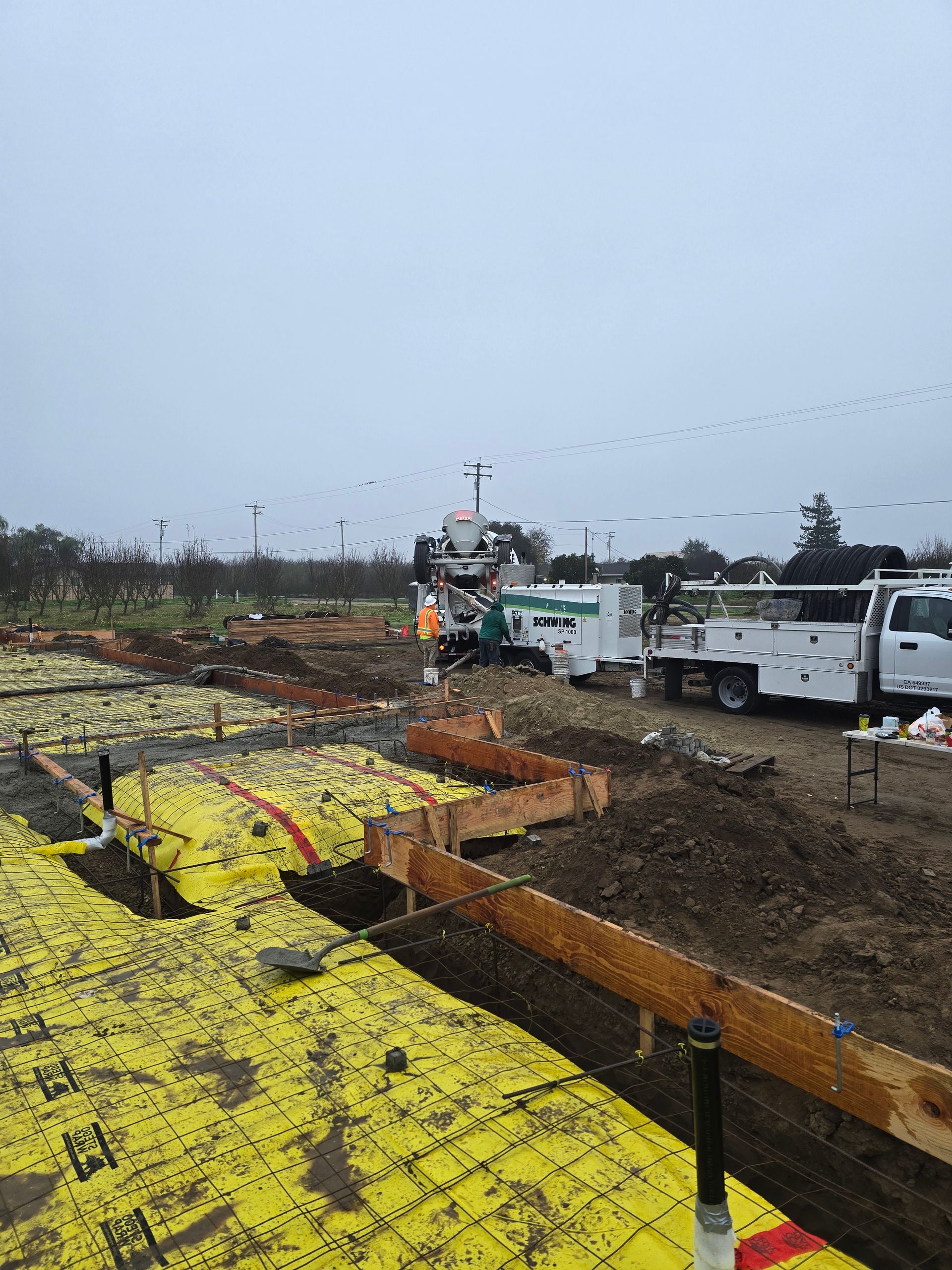Construction site with exposed trenches, yellow safety mesh, and utility trucks under an overcast sky