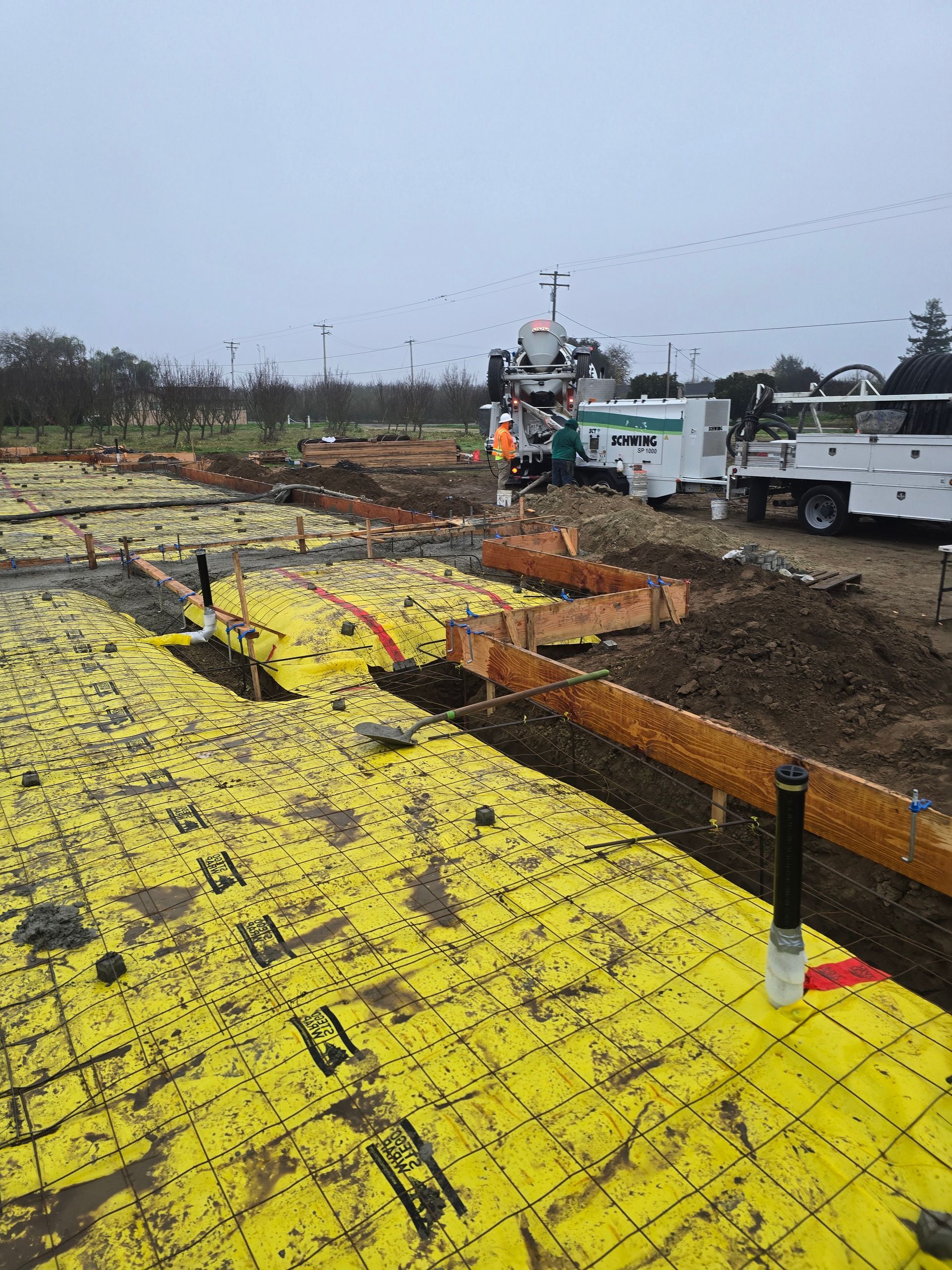 Storm-damaged roof with yellow tarp, debris, and utility trucks in a muddy yard