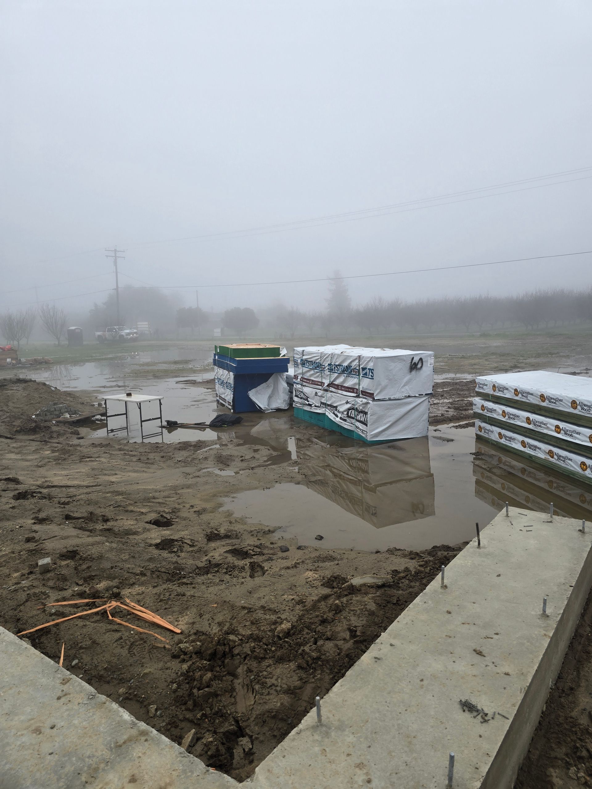 Foggy muddy construction site with concrete barriers, puddles, and a white tarp-covered structure