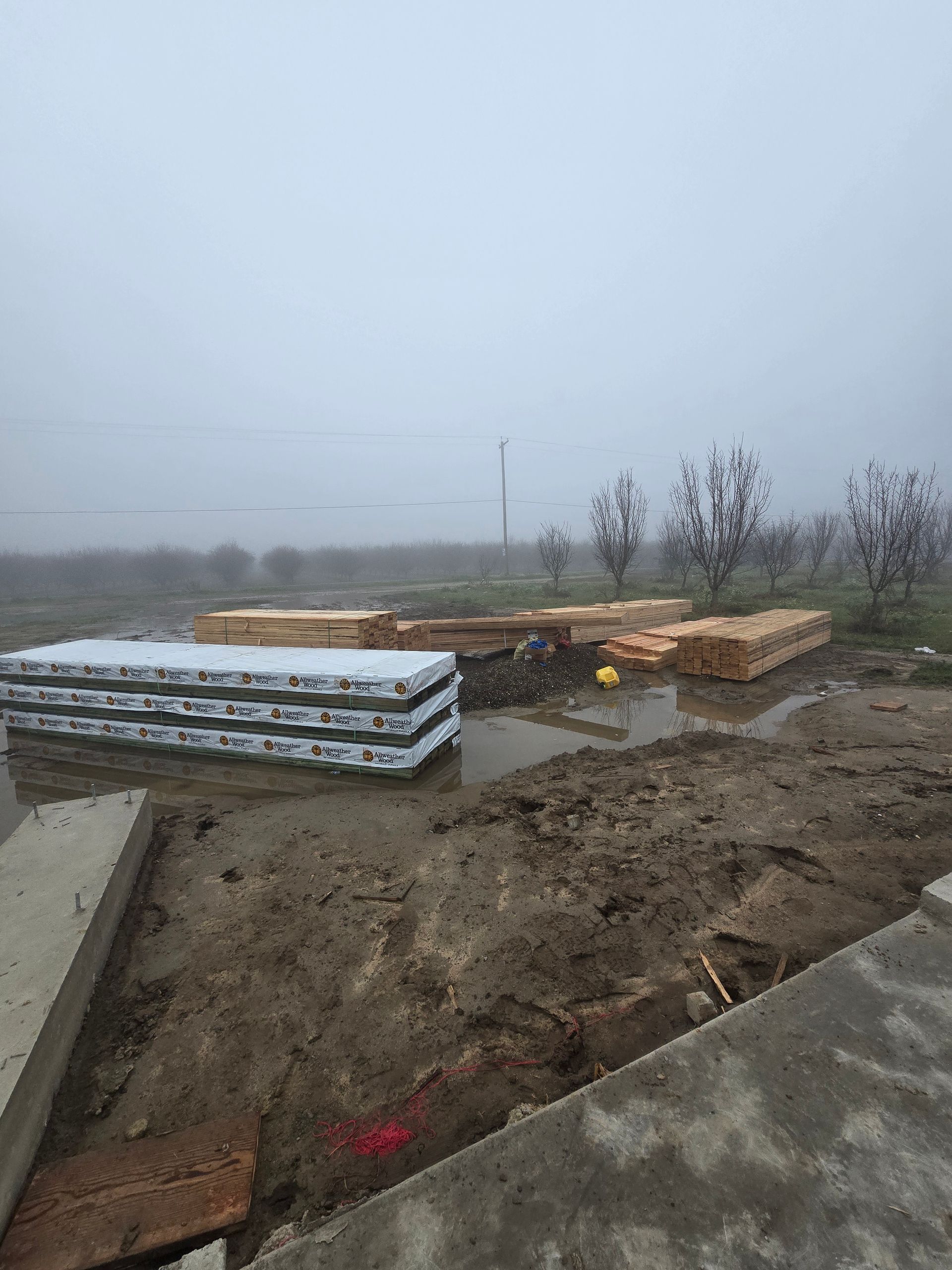 Foggy construction site with stacked materials, muddy ground, and concrete edges