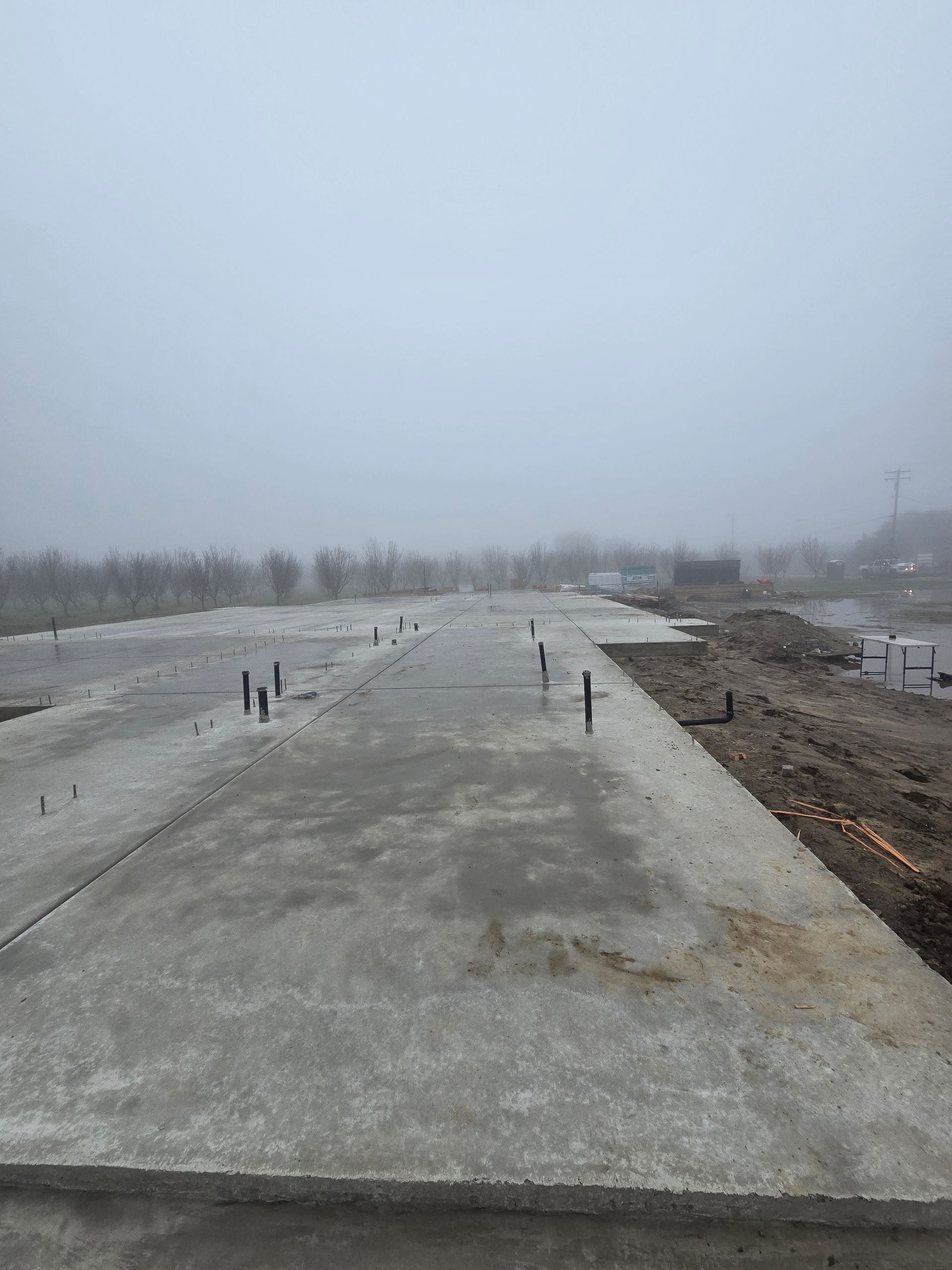 Concrete slab under construction in a foggy landscape, with rebar protruding along the edges.