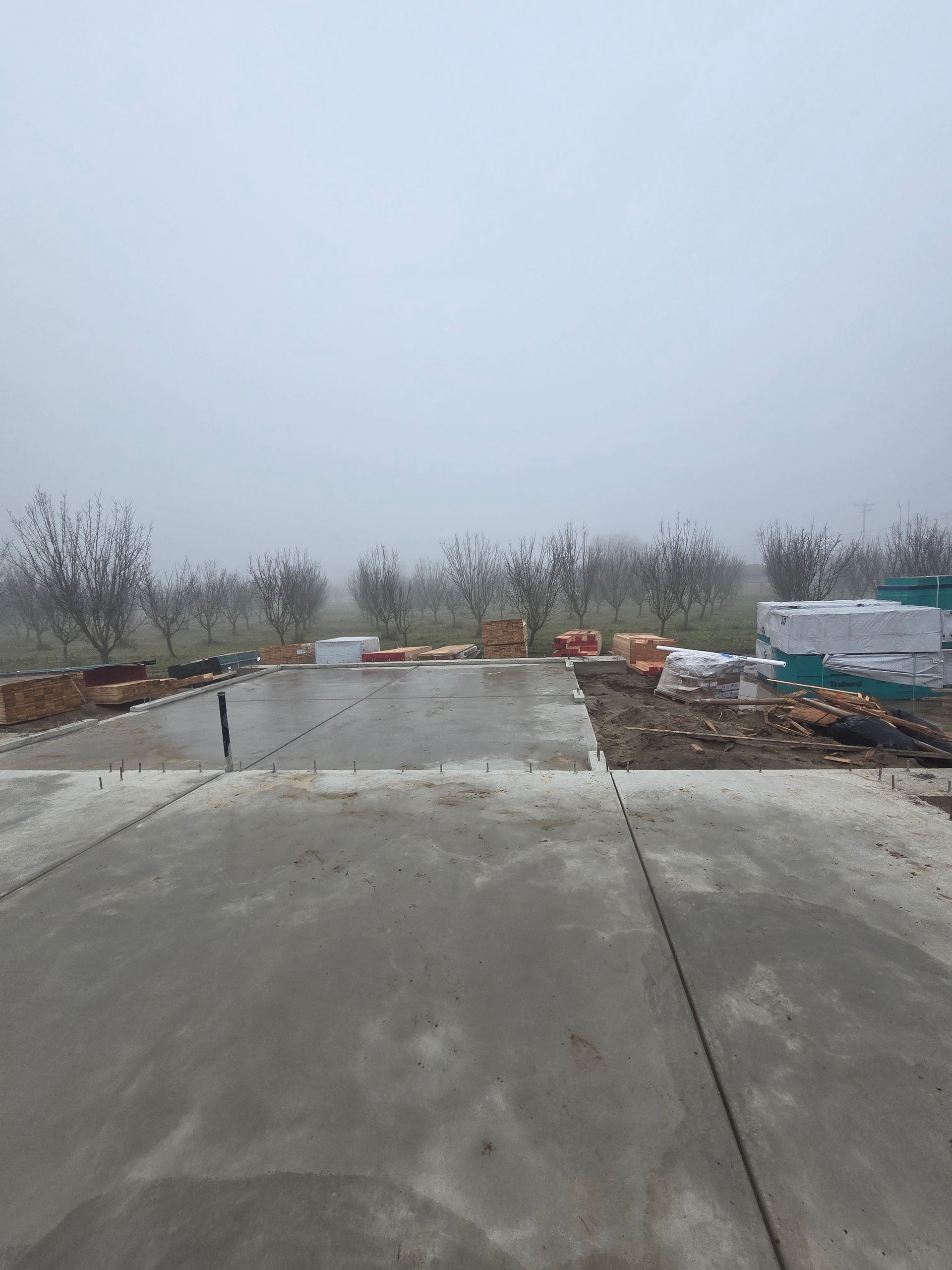 Wet concrete driveway leading to a barren outdoor lot under a gray sky