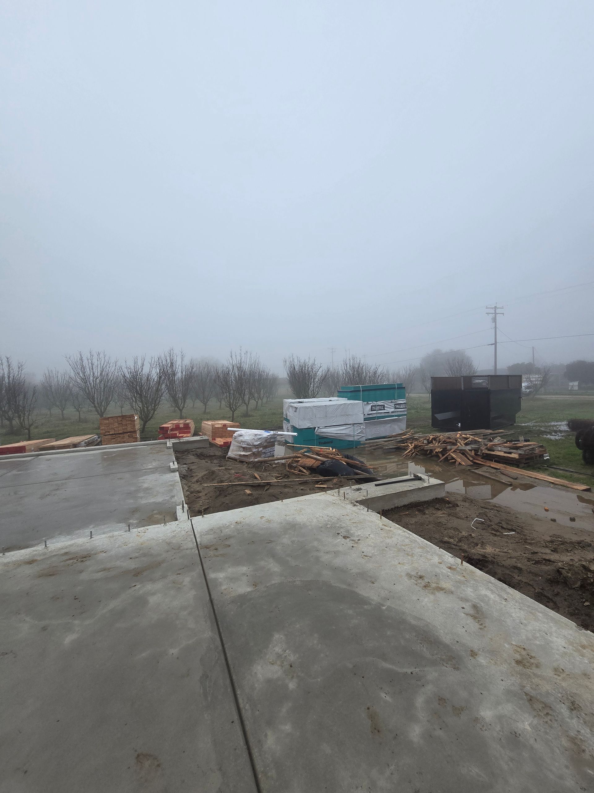 Foggy construction site with concrete pavement, dirt piles, and barriers along a roadside