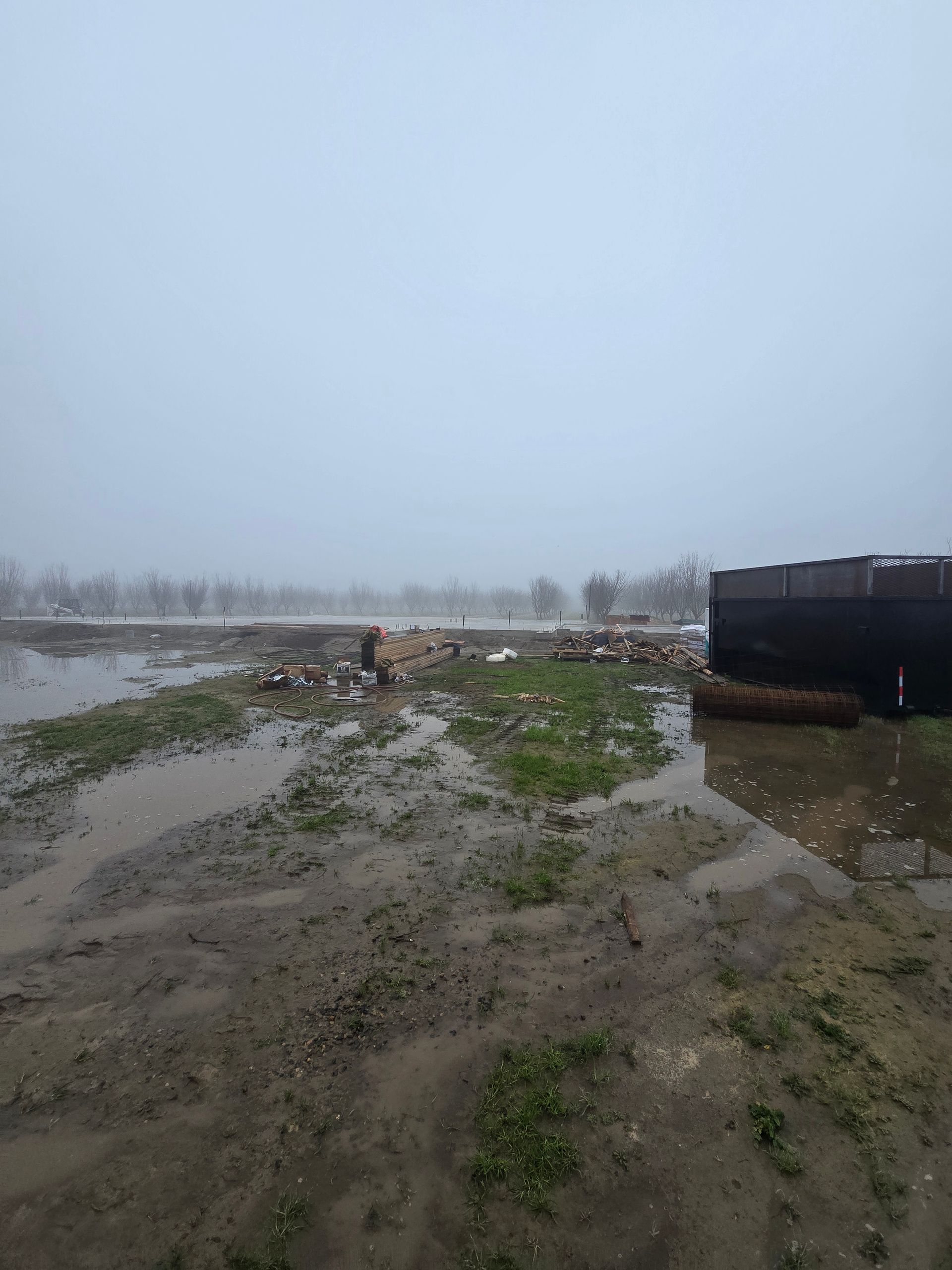 Flooded muddy shoreline with debris and a dark structure on the right under an overcast sky