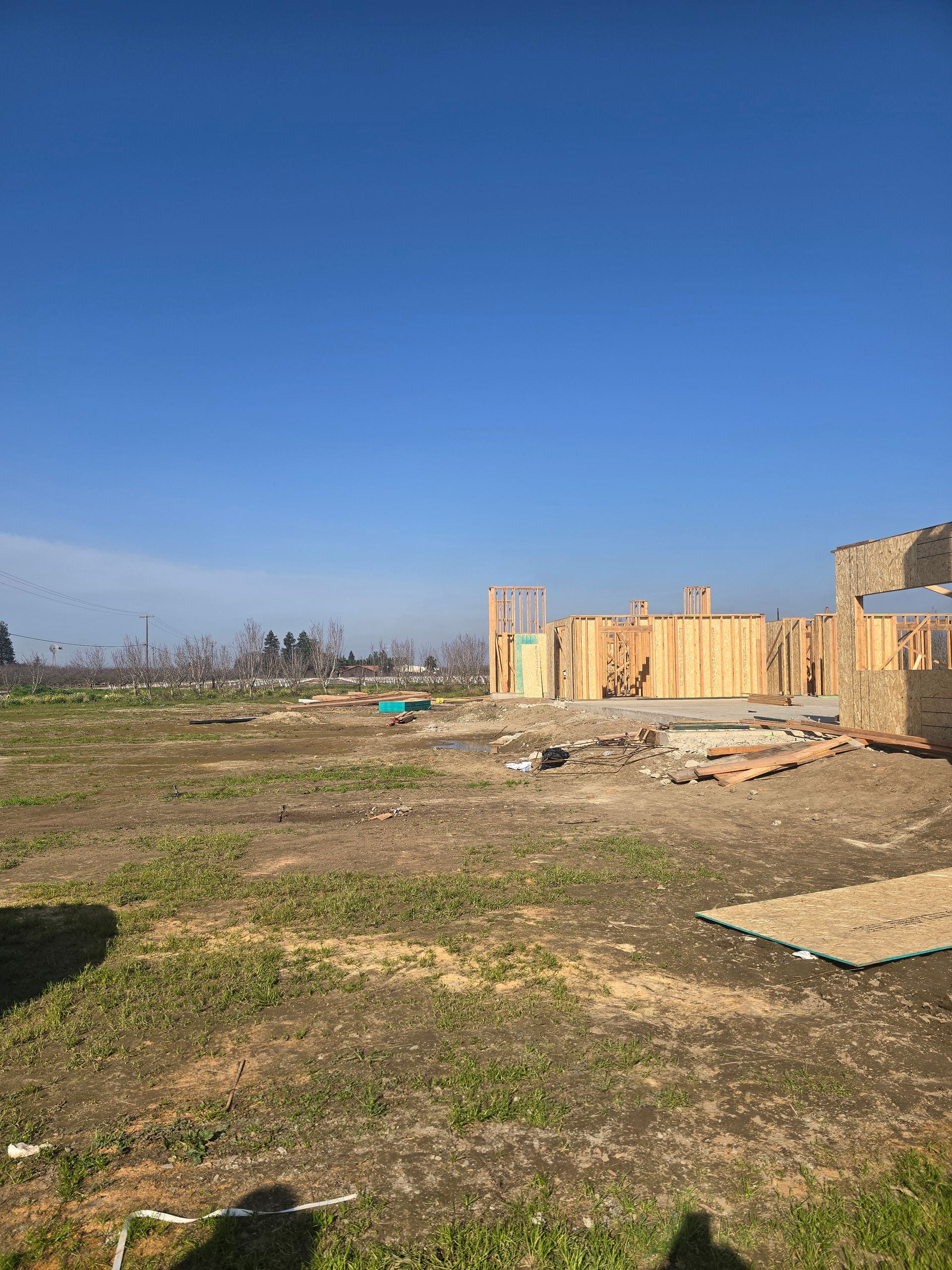 Open field with scattered debris and a partially built wooden structure under a clear blue sky