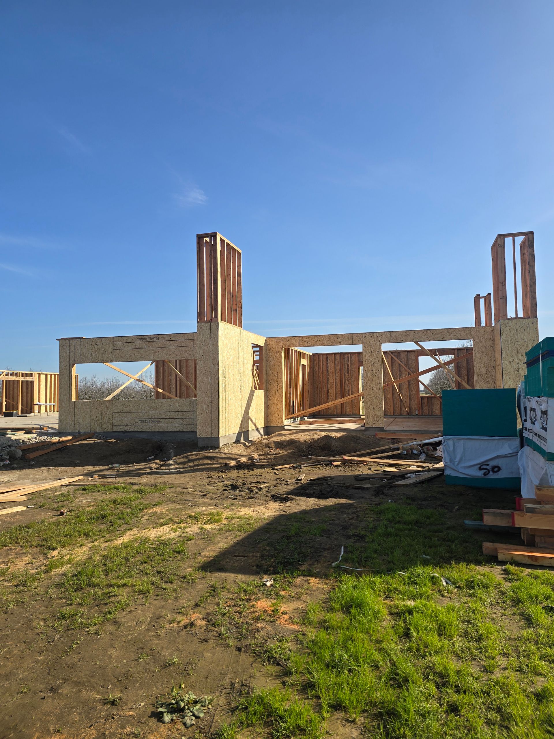 Partially built house frame with brick walls and tall columns under a clear blue sky