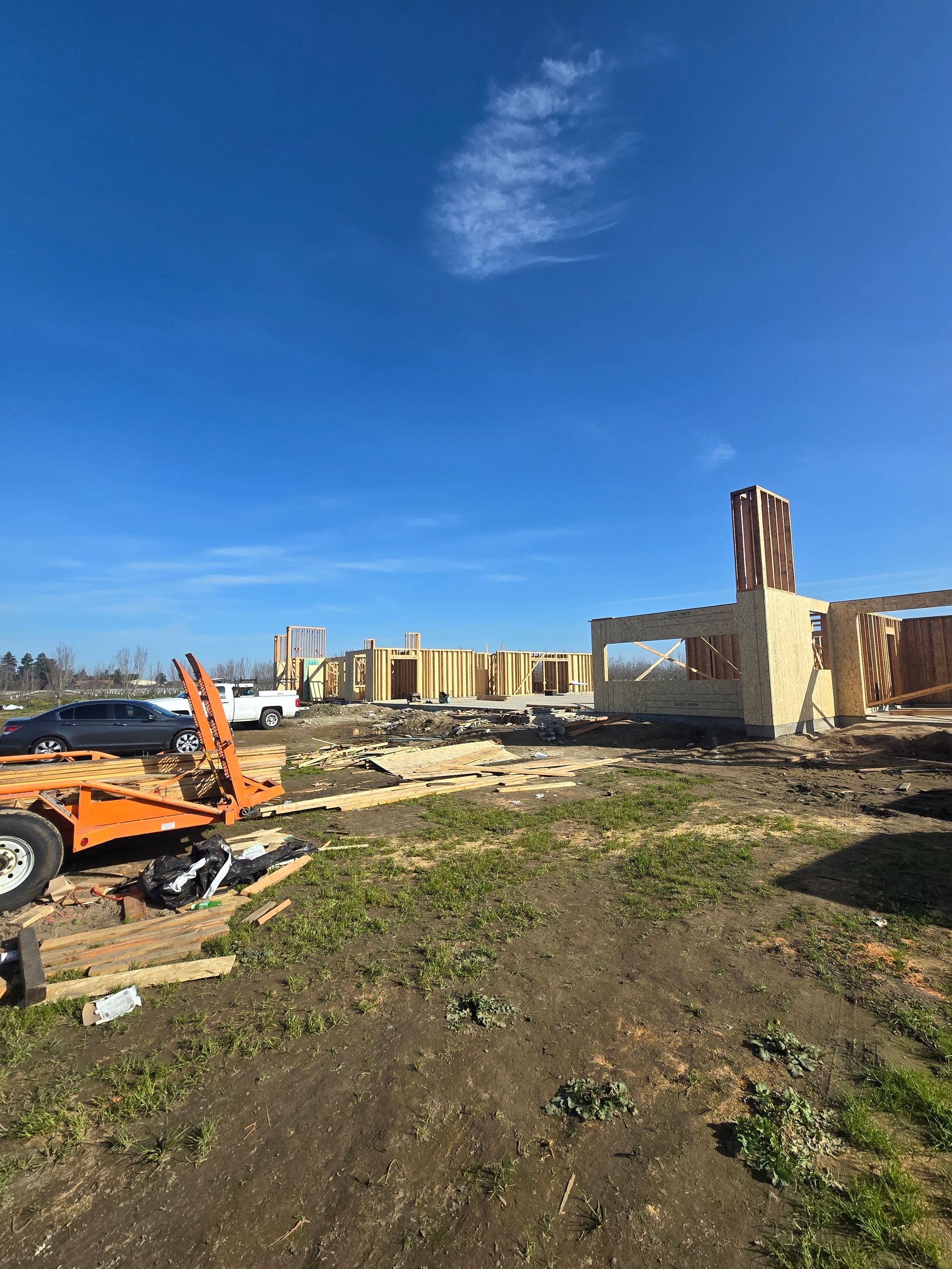 Construction site with rubble, an orange excavator, and unfinished buildings under a blue sky