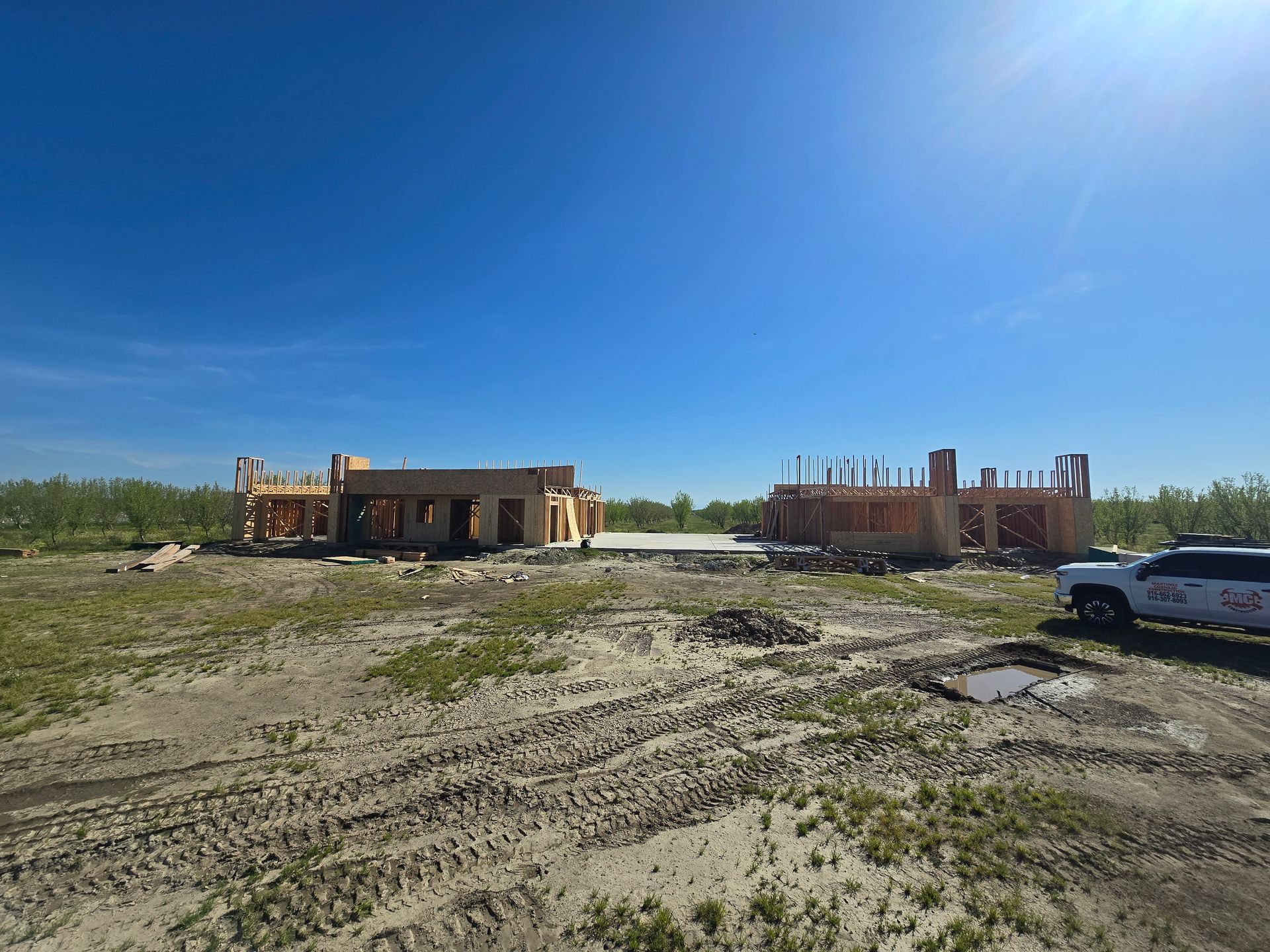 Partially built houses on a muddy construction site under a bright blue sky