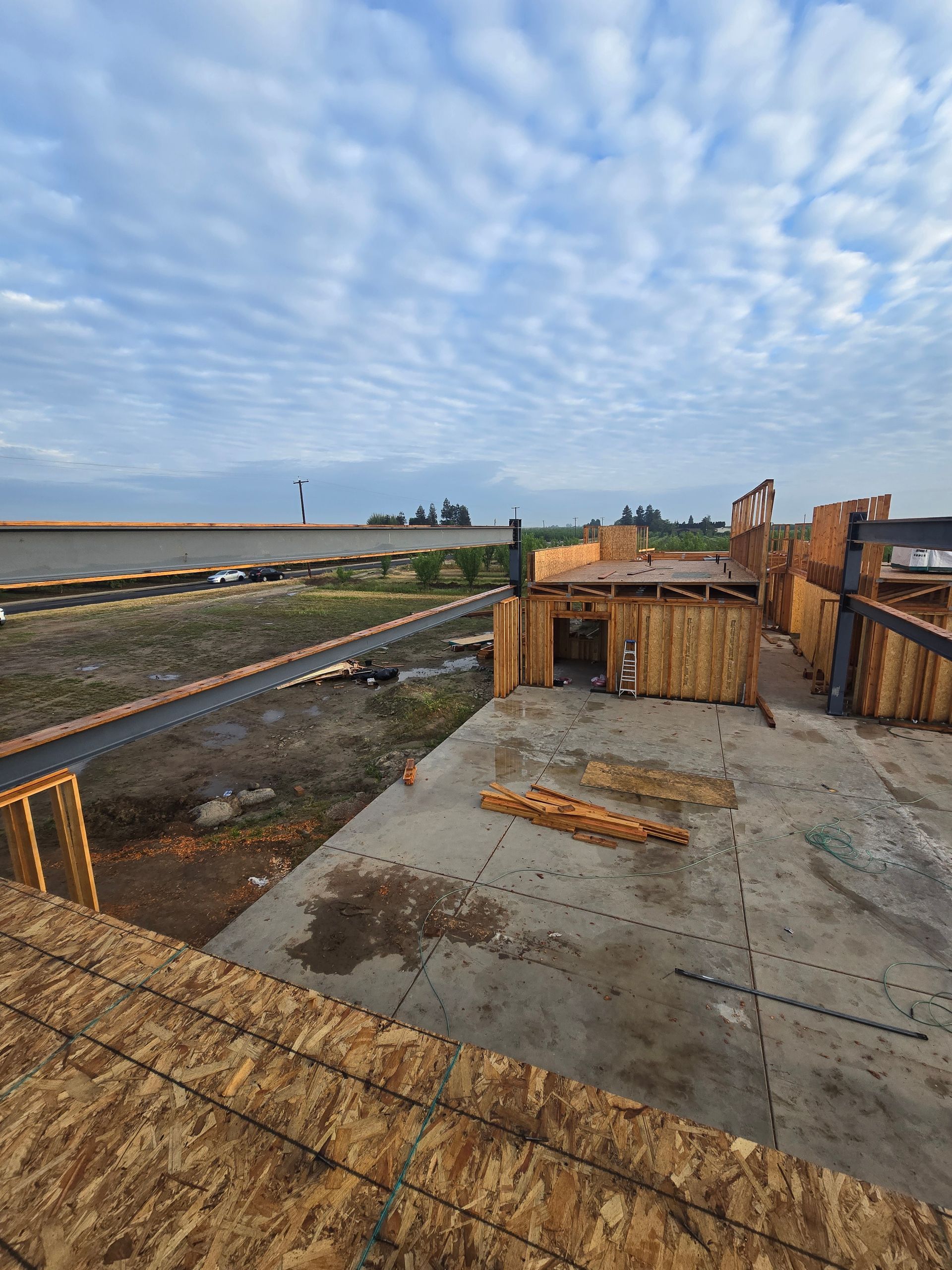 Construction site with concrete foundation forms, wooden framing, and a cloudy sky over open land