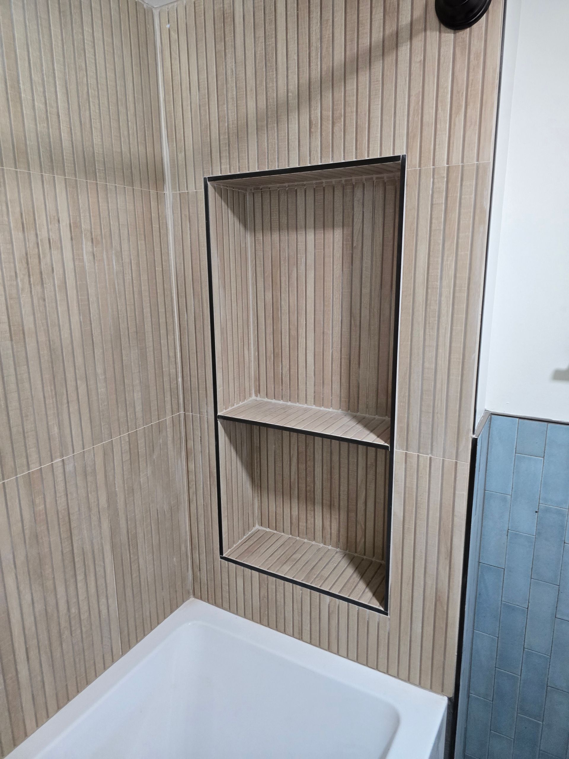 Bathroom wall niche with two shelves, framed in dark trim, above a white tub and blue tile.