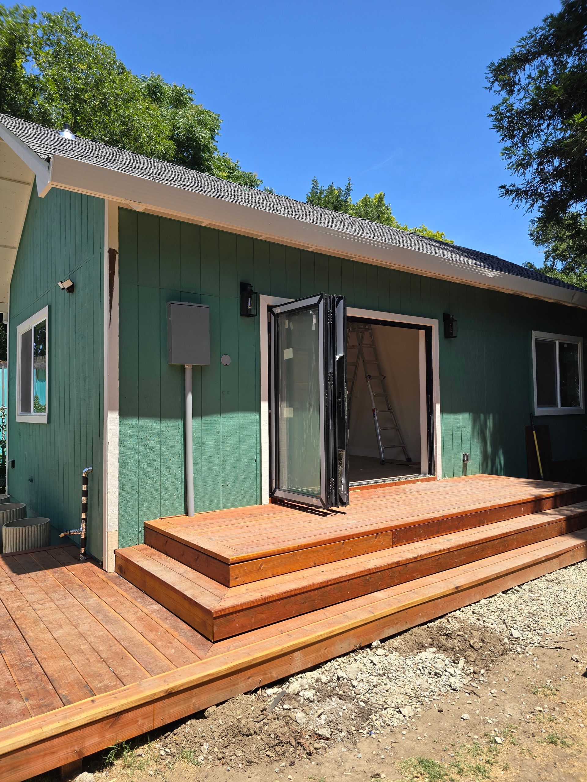 Green house exterior with open glass doors and a wooden deck under a sunny blue sky