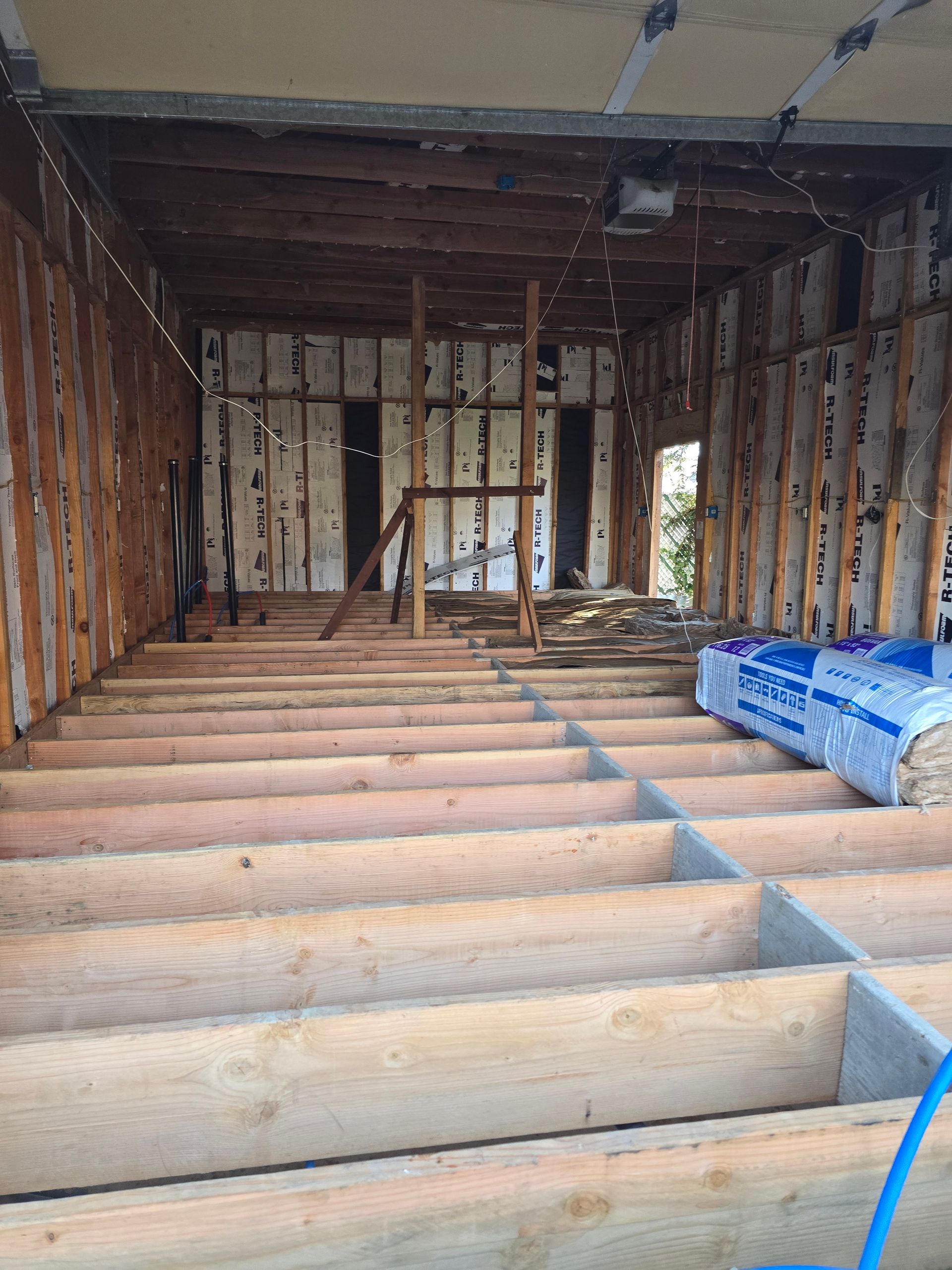 Interior of a house under construction with exposed framing, floor joists, and stacked insulation bundles