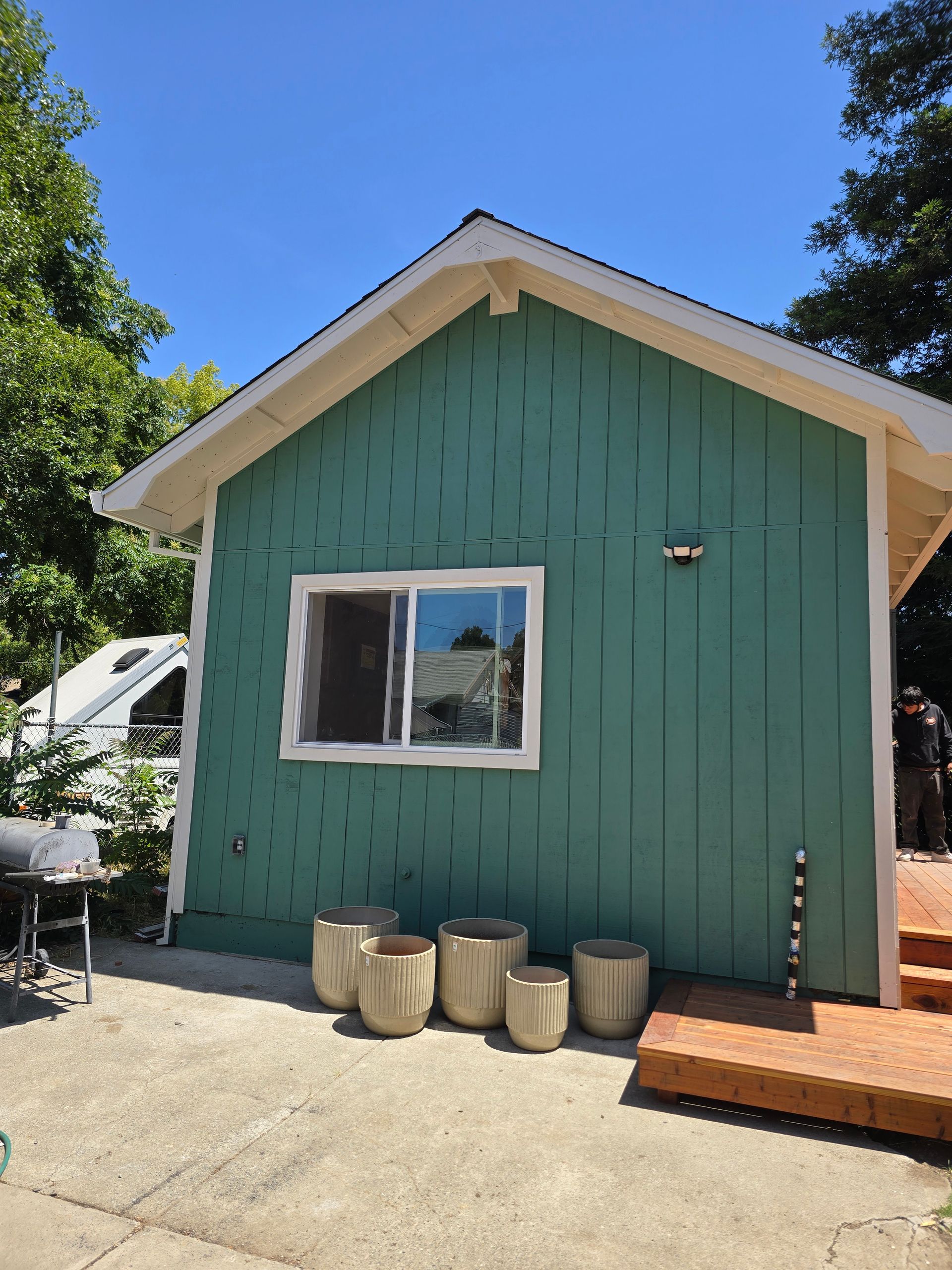Teal cottage with white trim, small window, potted jars, and brick steps under a blue sky.