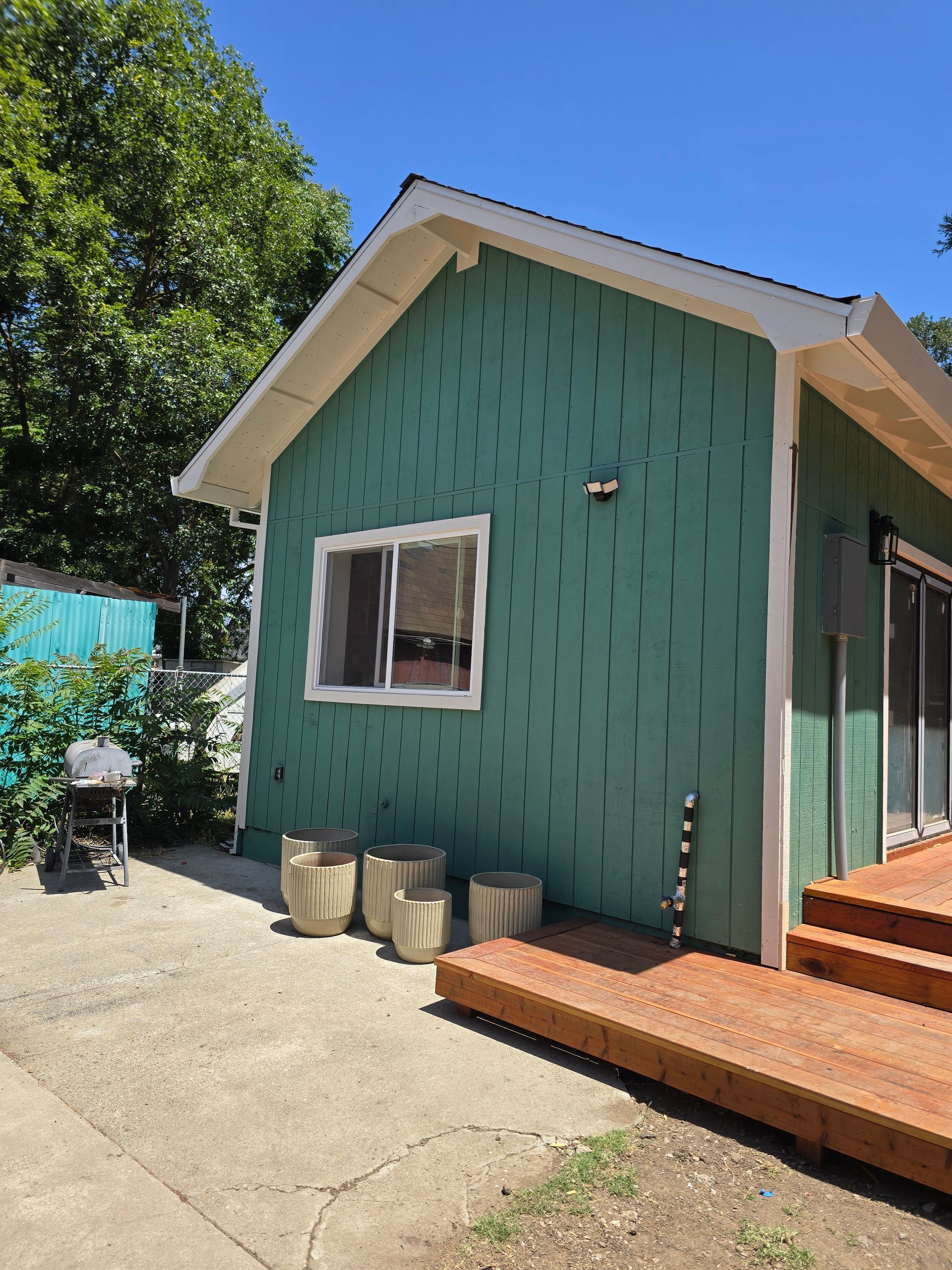 Green house exterior with wooden deck, window, and concrete patio under a clear blue sky