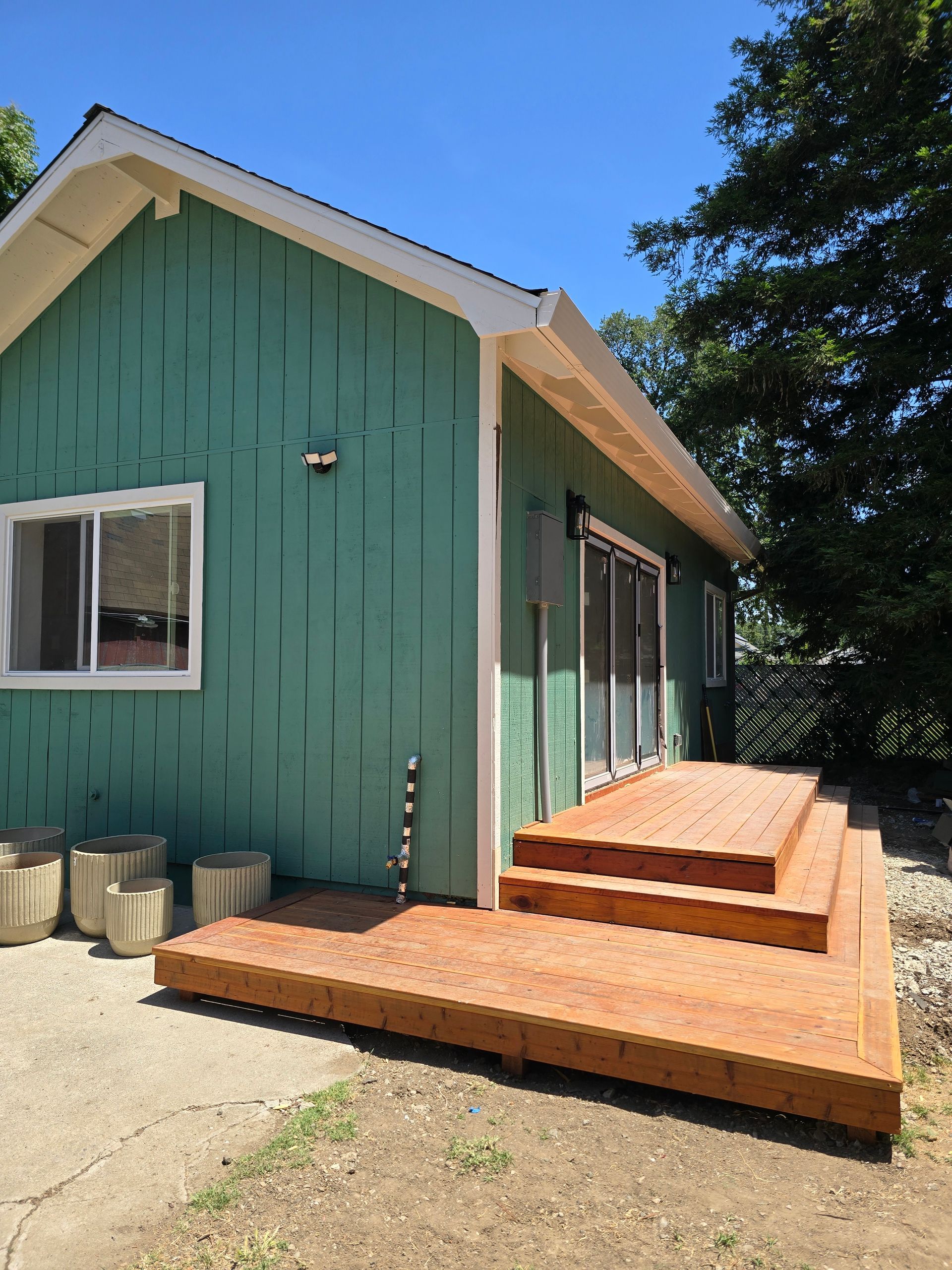 Green house exterior with wood steps and a small deck under a blue sky