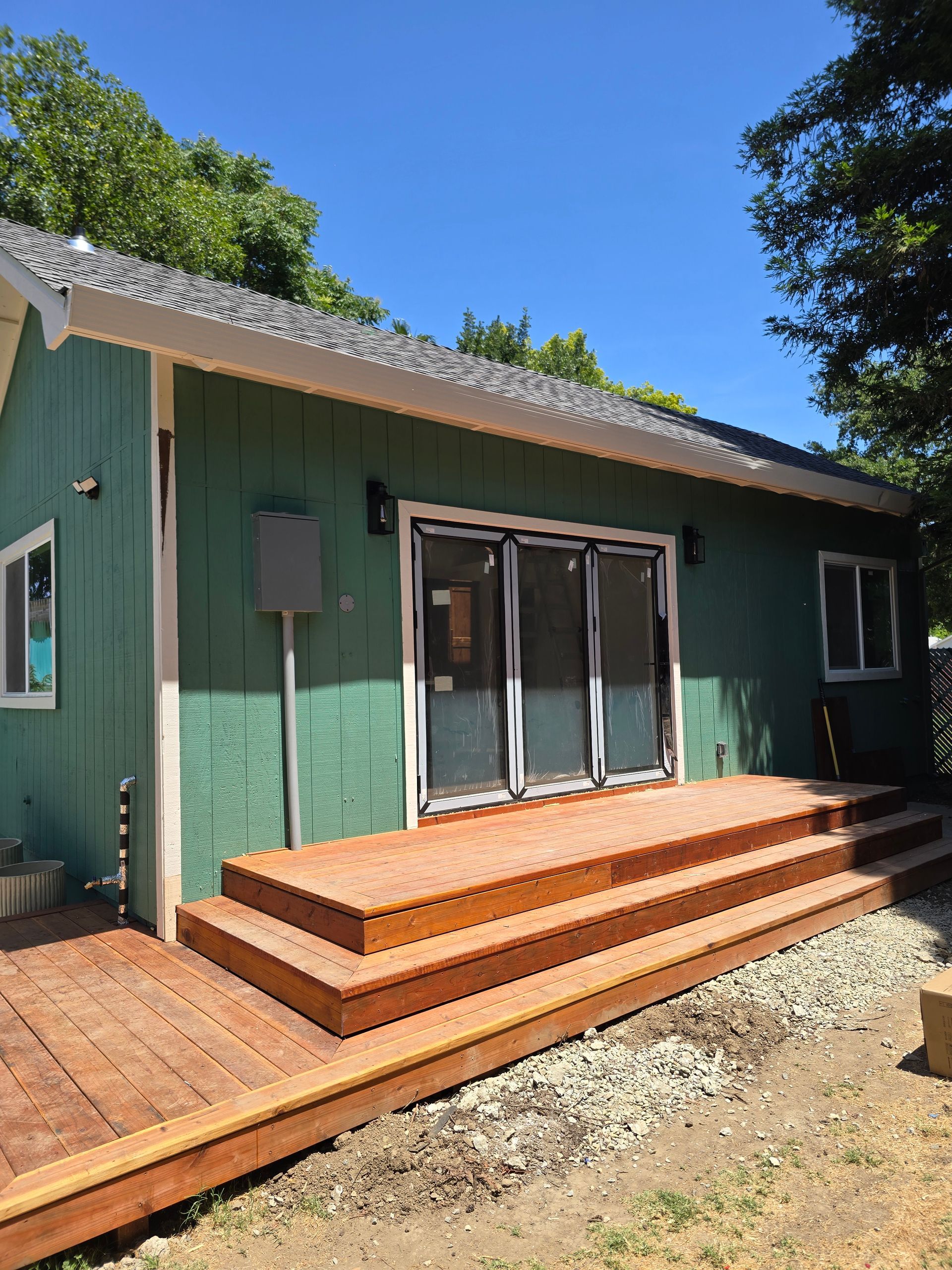 Green house with double glass doors, wooden deck steps, and a blue sky overhead
