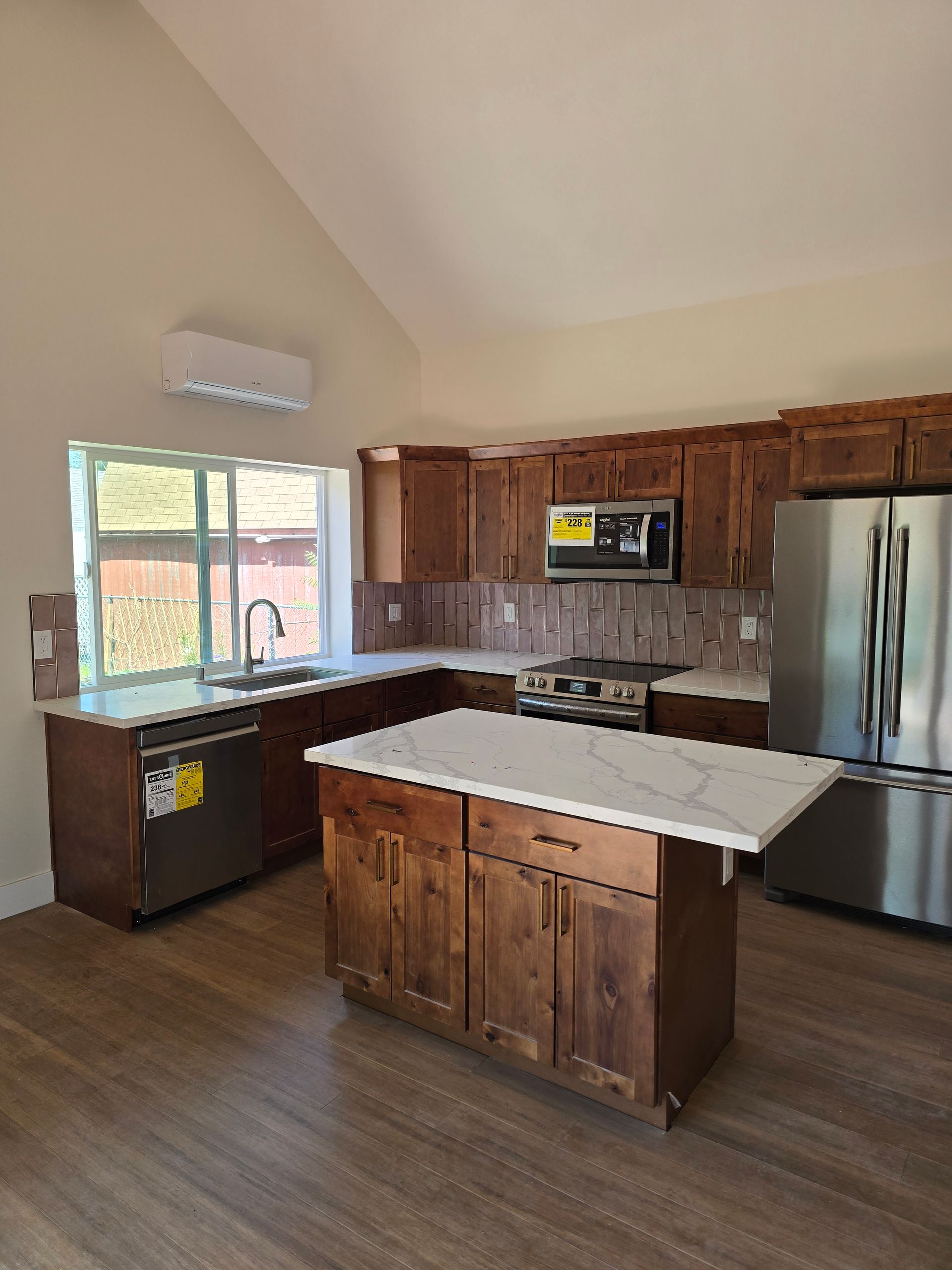 Modern kitchen with wood cabinets, stainless steel fridge, white island, and a large window