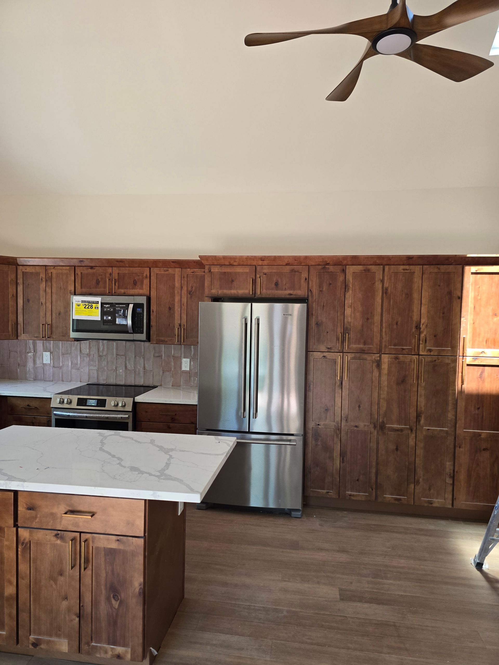 Modern kitchen with wood cabinets, stainless steel fridge, marble island, and ceiling fan