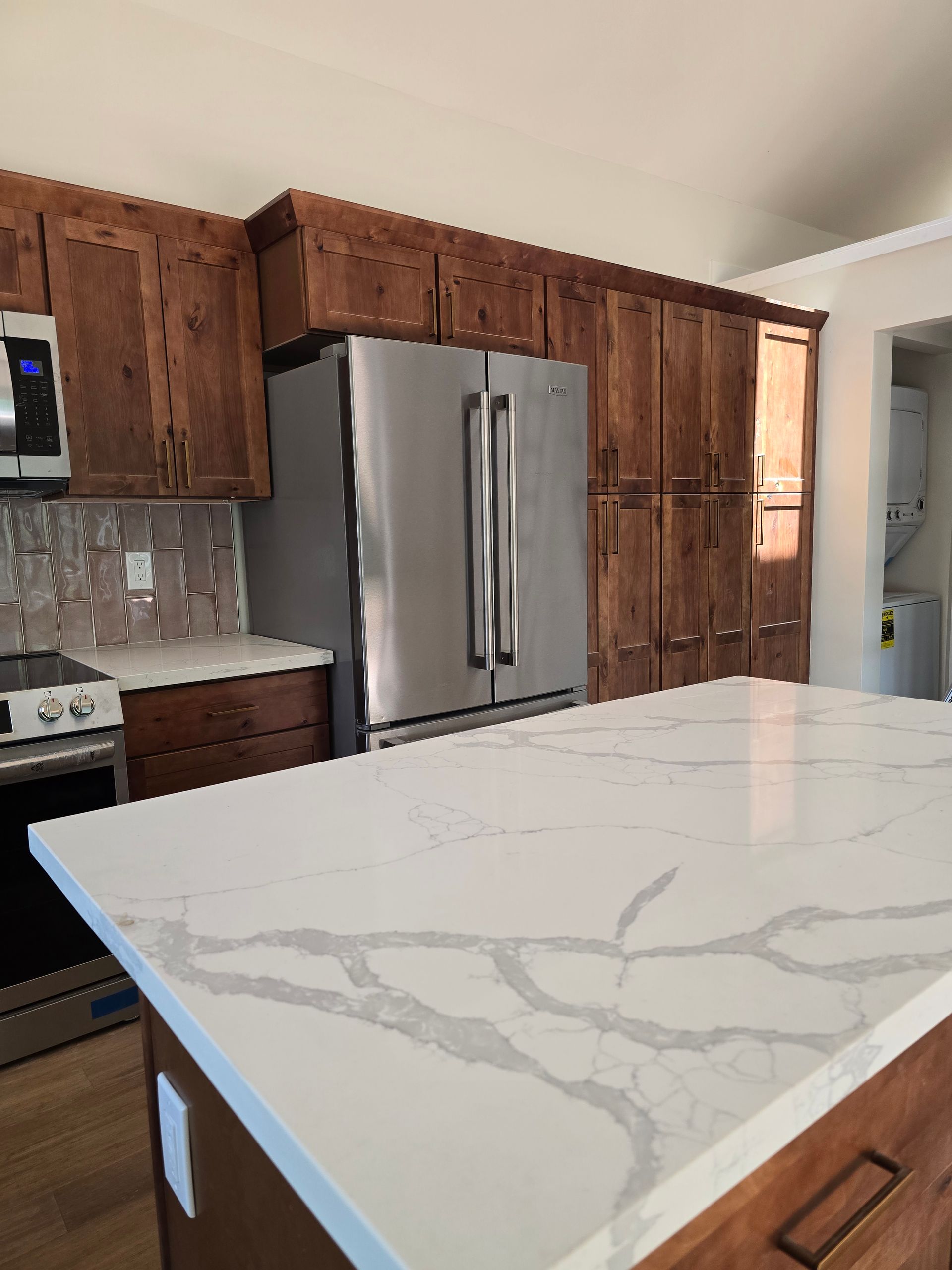 Modern kitchen with stainless steel fridge, wood cabinets, and a white marble-pattern island countertop