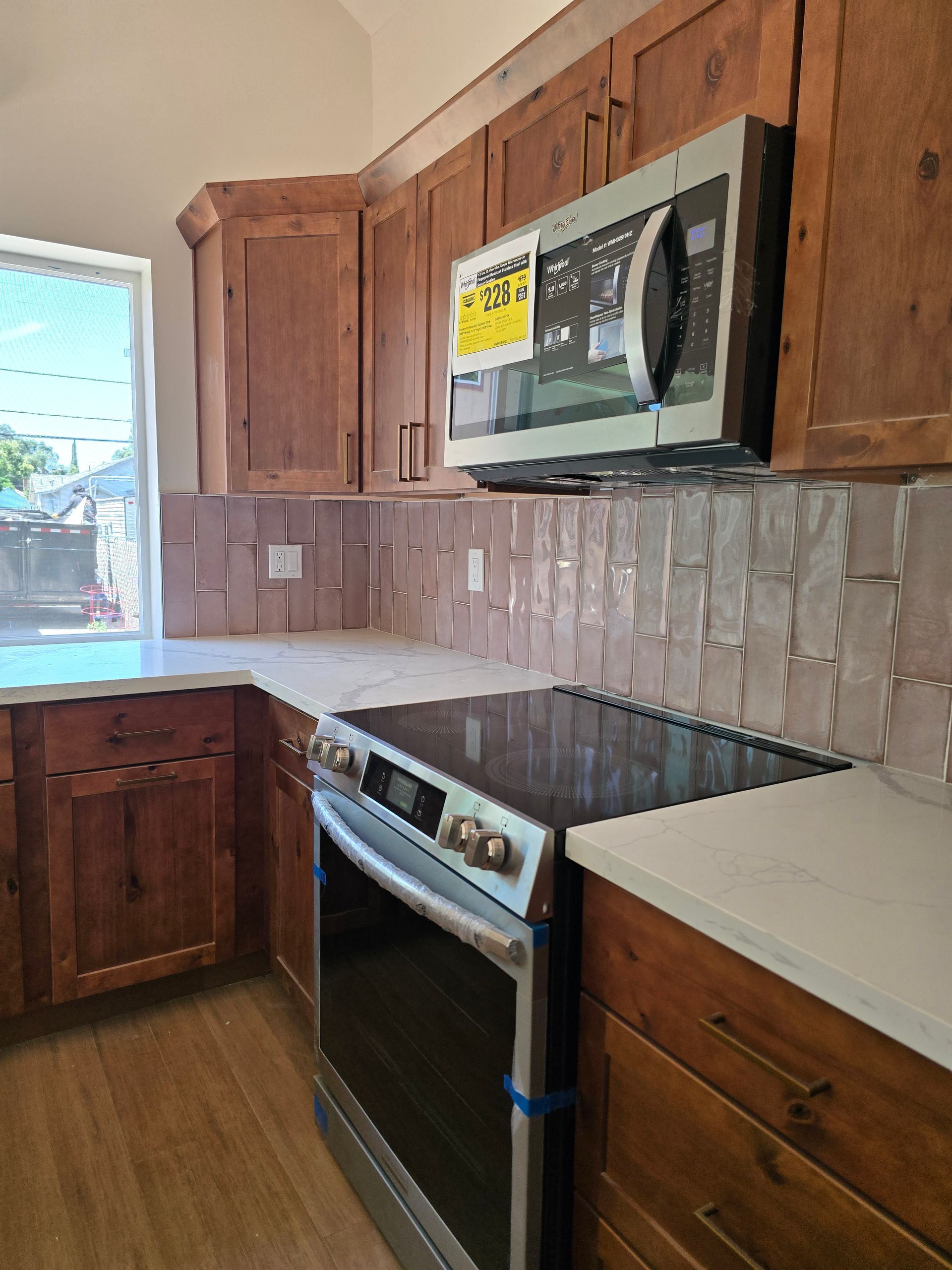 Small kitchen with wood cabinets, white countertops, tiled backsplash, stove, microwave, and window.