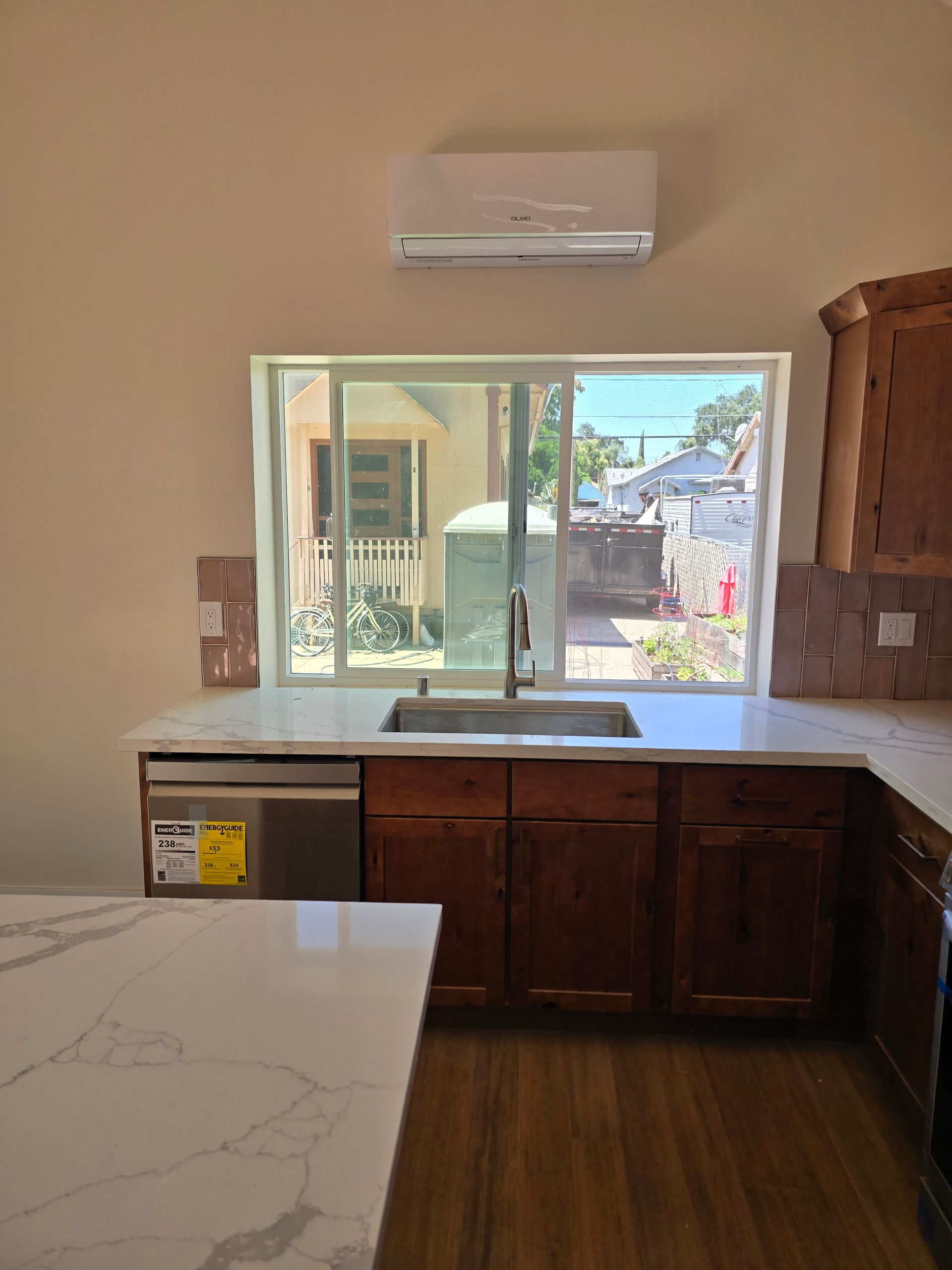 Empty kitchen with white island, wood cabinets, sink under a window, and wall-mounted air conditioner