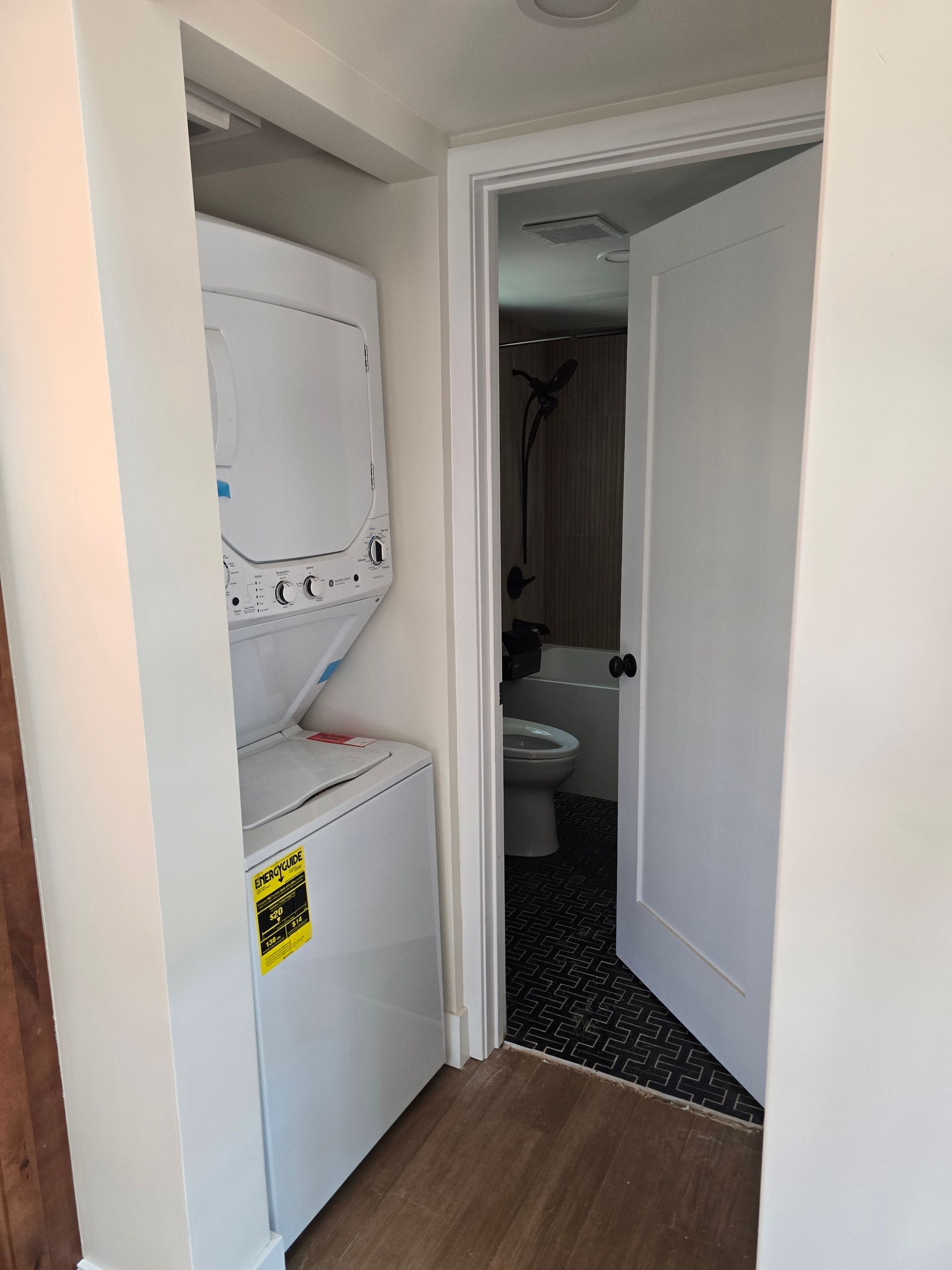 Laundry closet with stacked washer and dryer beside a narrow hallway and bathroom.