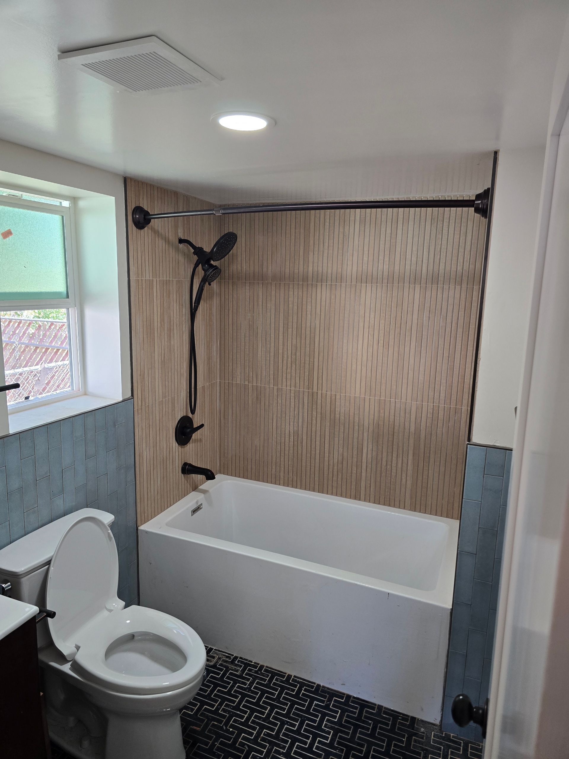 Bathroom with toilet, tub, and showerhead, featuring beige wall panels and black-and-white floor tiles