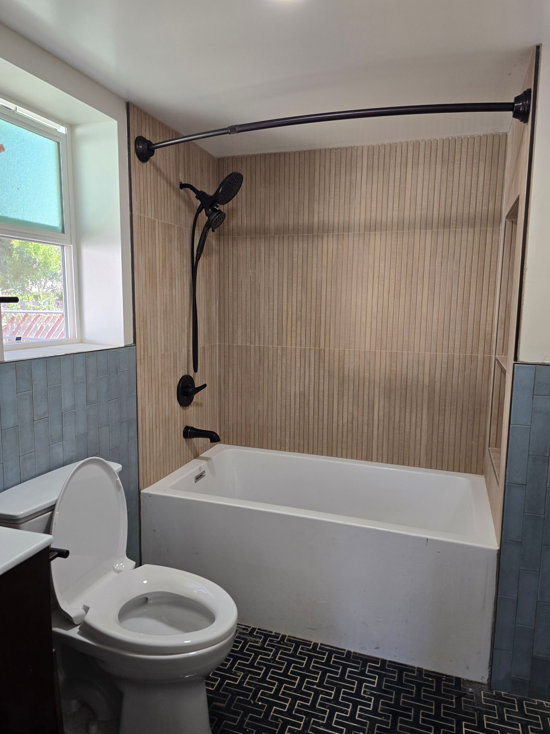 Bathroom with toilet, bathtub, and black shower fixture beside a window.