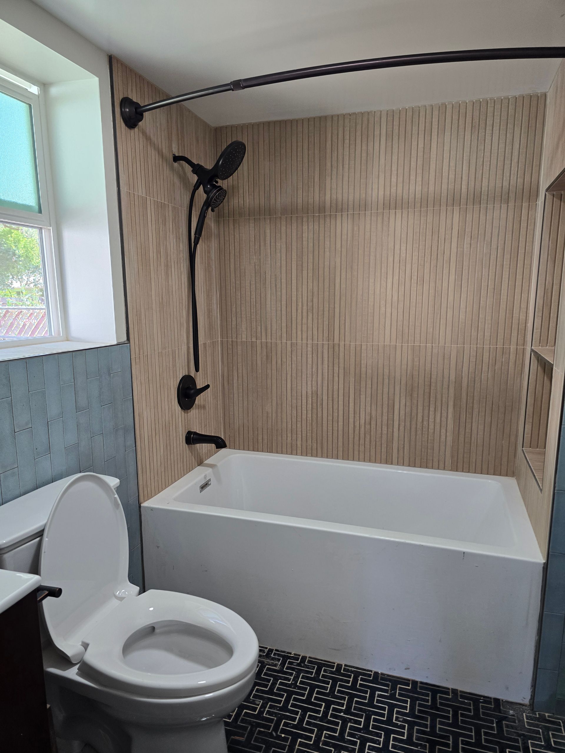Bathroom with toilet and bathtub, shower head, bamboo wall panel, and tiled floor.