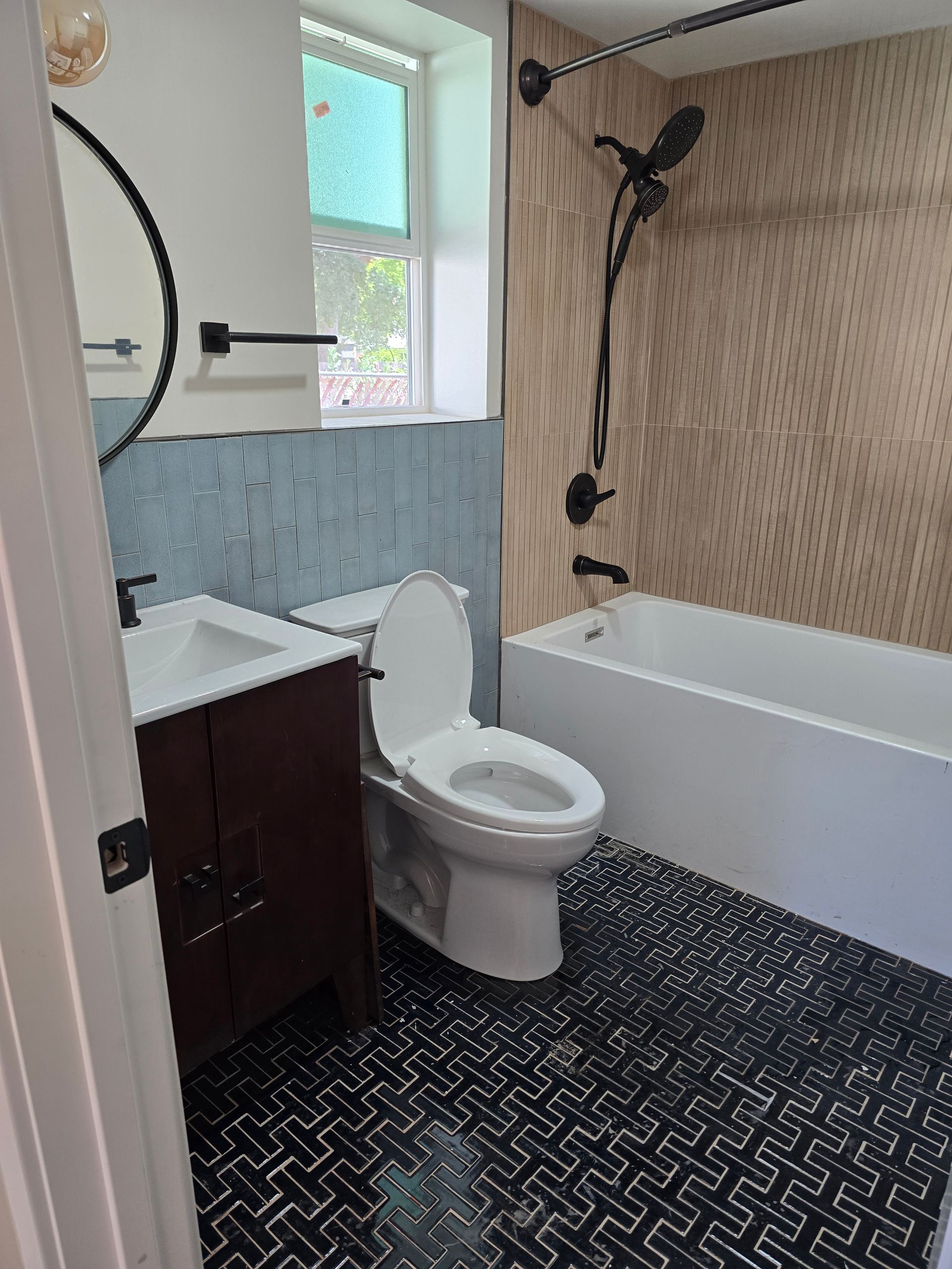 Small bathroom with white toilet, vanity, shower, patterned wallpaper, and dark herringbone floor.