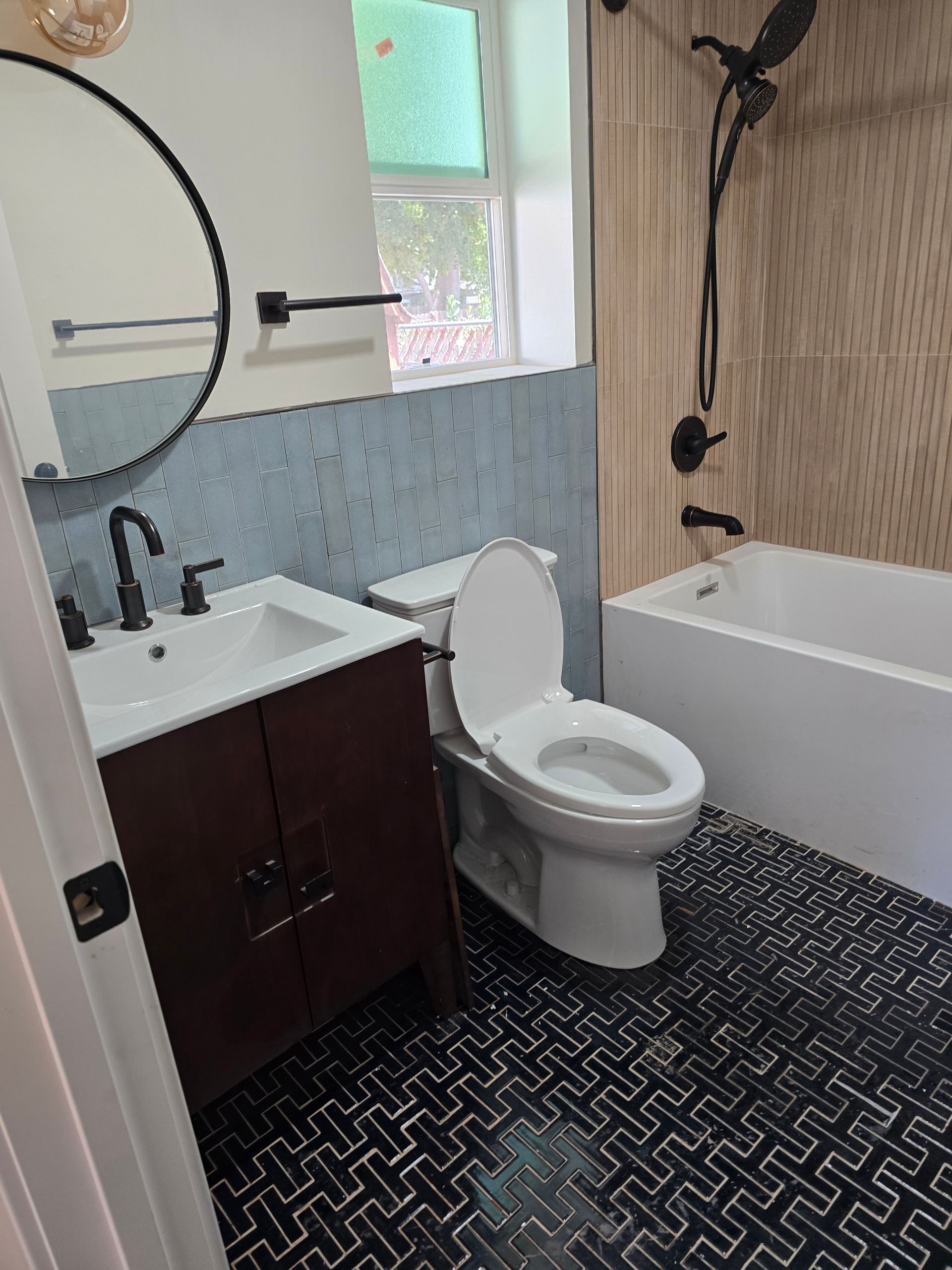 Small bathroom with vanity, toilet, tub, and black-and-white herringbone floor.
