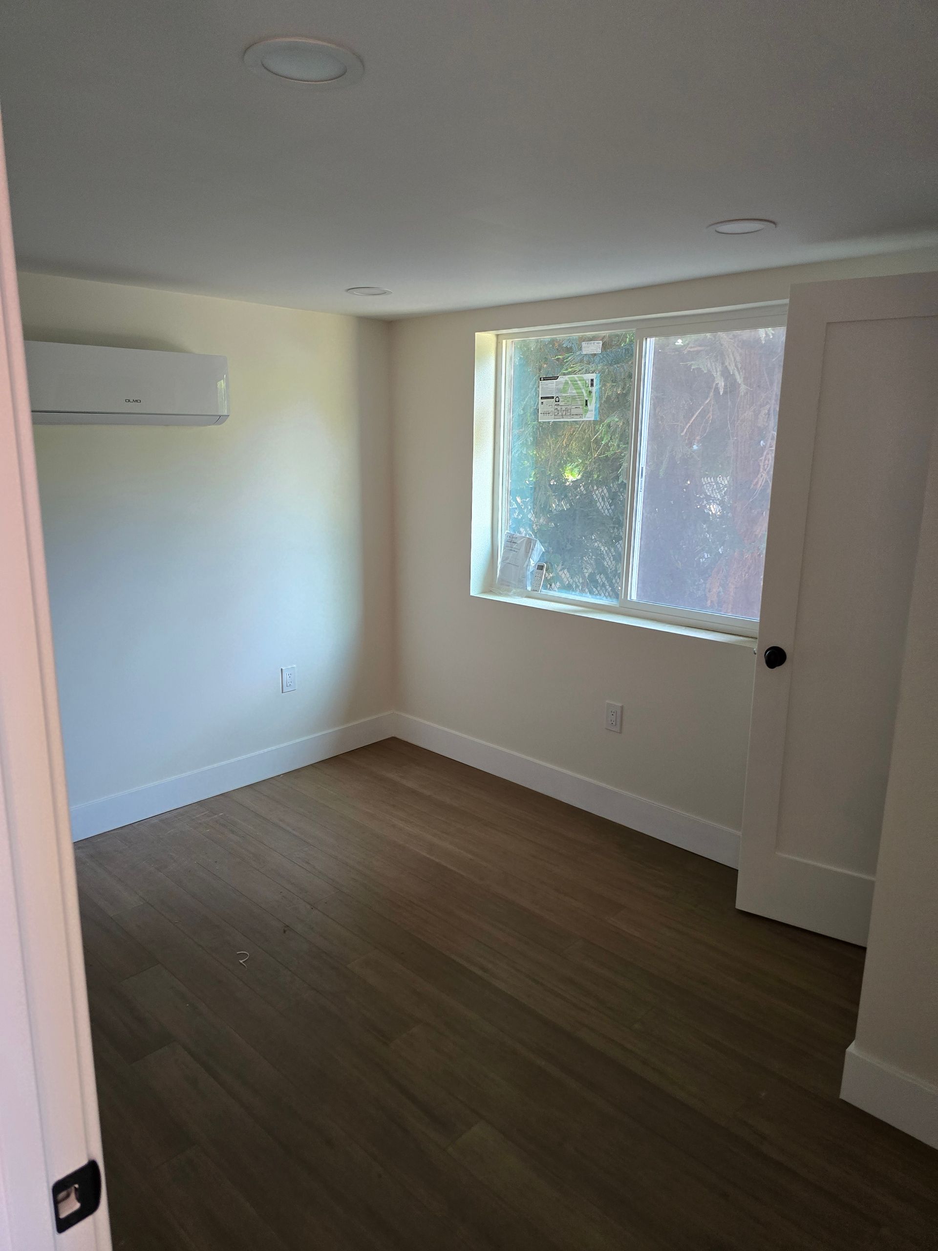 Empty white bedroom with wood floor, large window, and closet door partially open
