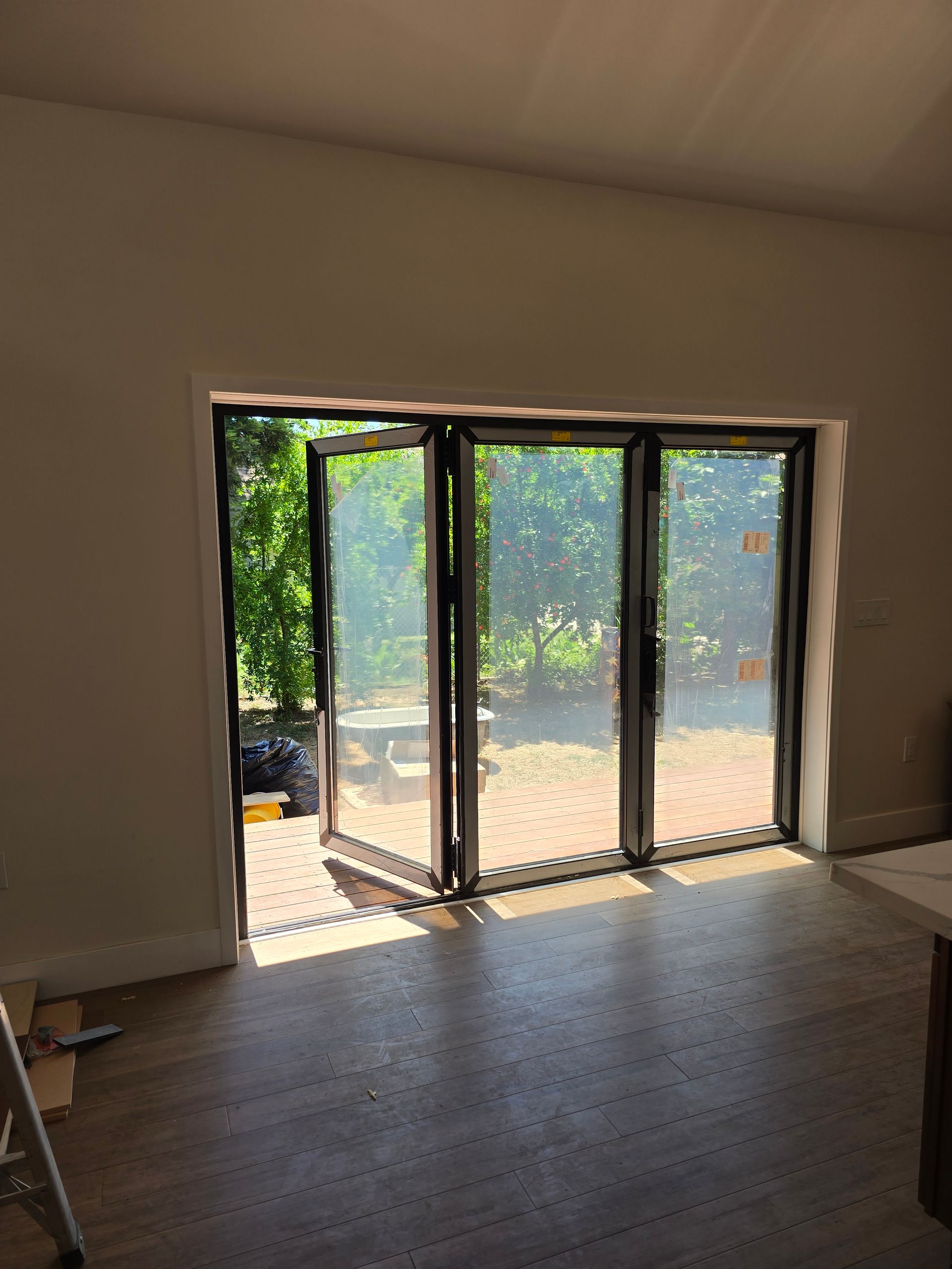 Sunlit empty room with large folding glass doors opening to a green patio