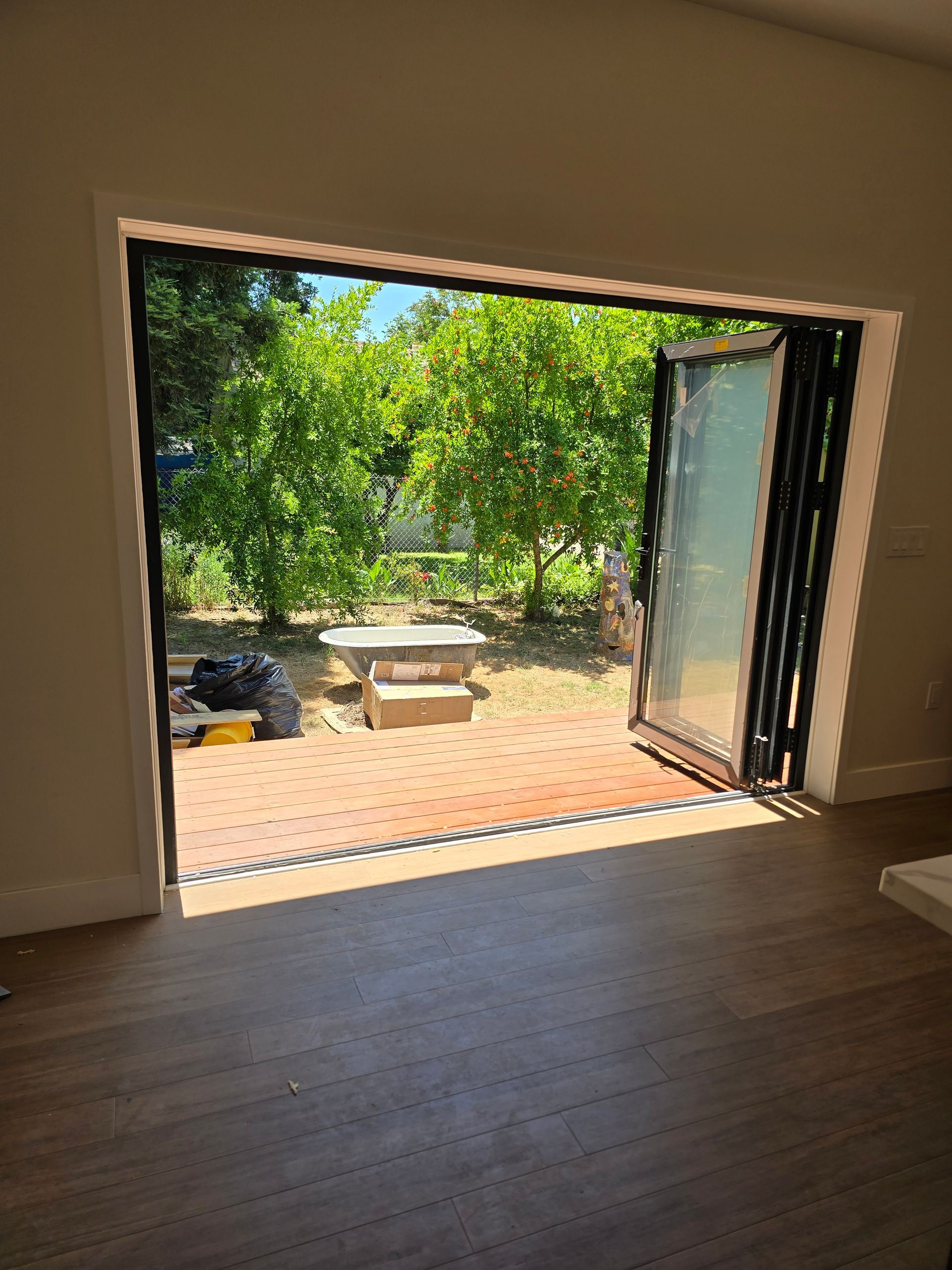 Open patio doors overlooking a sunny garden with trees and a stone bench.