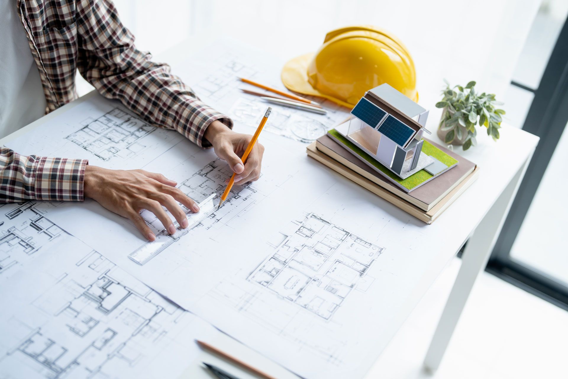 Architect reviewing house blueprints with pencils, hard hat, and scale model on a desk