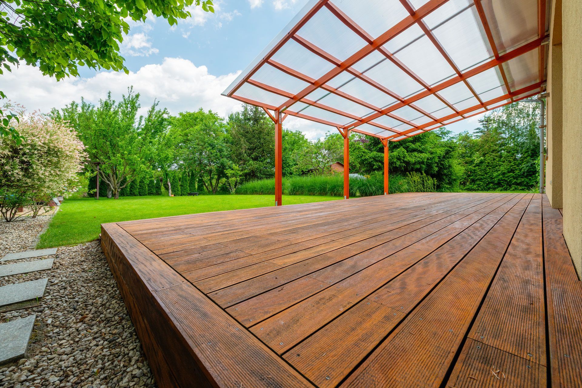 Wooden deck under a red pergola beside a green garden and stone steps