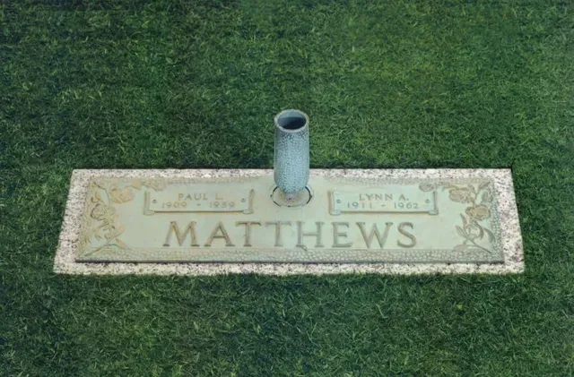 Flat cemetery marker engraved “MATTHEWS” on grass with a small vase holder.