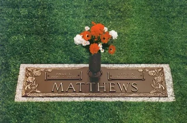Gravestone marker with “MATTHEWS” and orange-white flowers on green grass