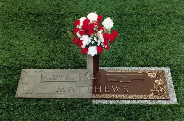 Gravestone with red and white flowers on green grass, marked MATTHEWS.