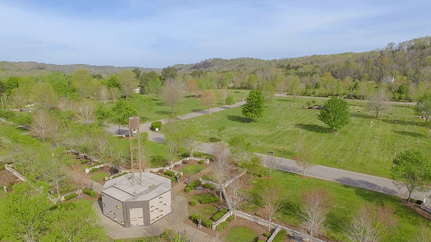 Aerial view of a green park with trees, paths, and a small pavilion under a blue sky