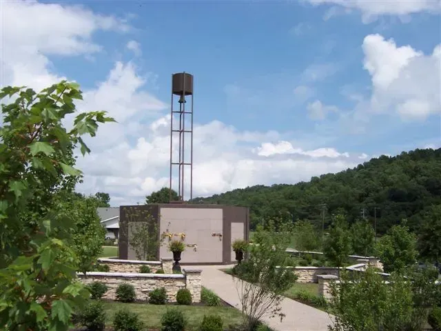 Rural building with a tall water tower, surrounded by greenery under a blue sky.