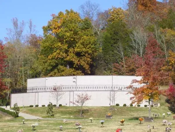 White circular building in a landscaped garden with autumn-colored trees in the background.