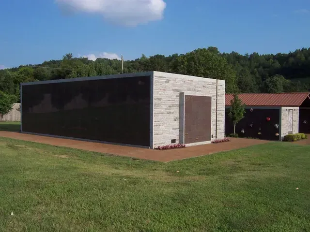 Small modern utility building with dark and light walls on a grassy lawn under a blue sky.
