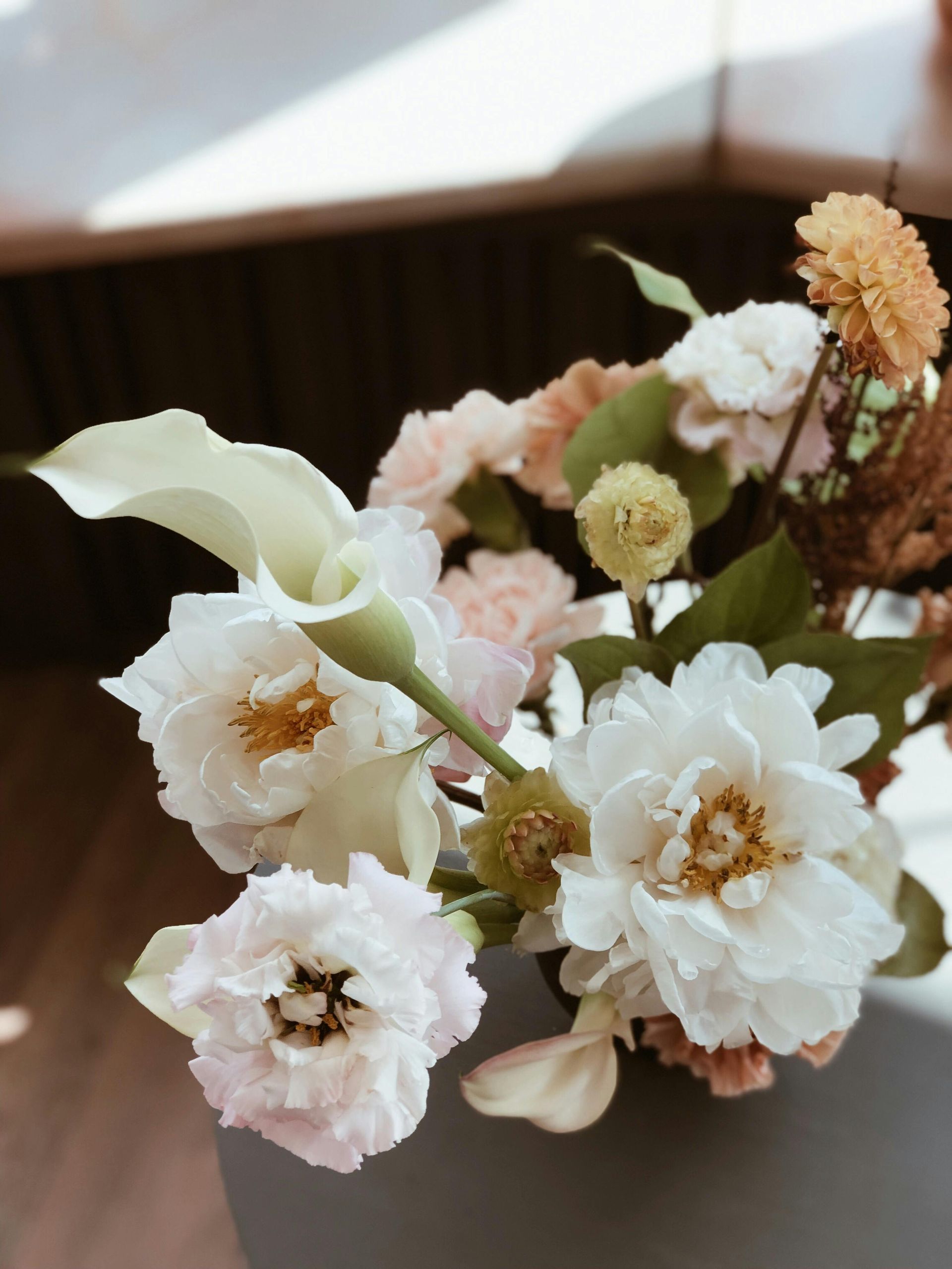 Bouquet of white and pale pink flowers with green leaves on a blurred indoor background