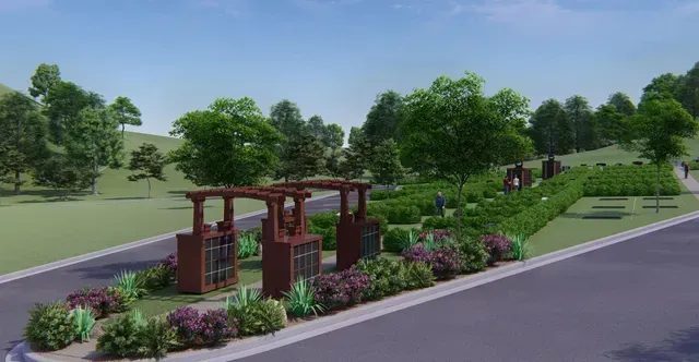 Landscaped roadside with flowering shrubs, pergola benches, and trees beside a paved street.