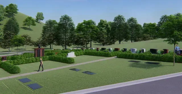 Park with trees, shrubs, benches, and a person walking along a paved path near the road.