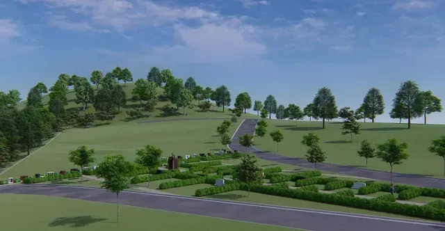 Landscaped park with grassy hills, trees, winding paths, and a road under a blue sky