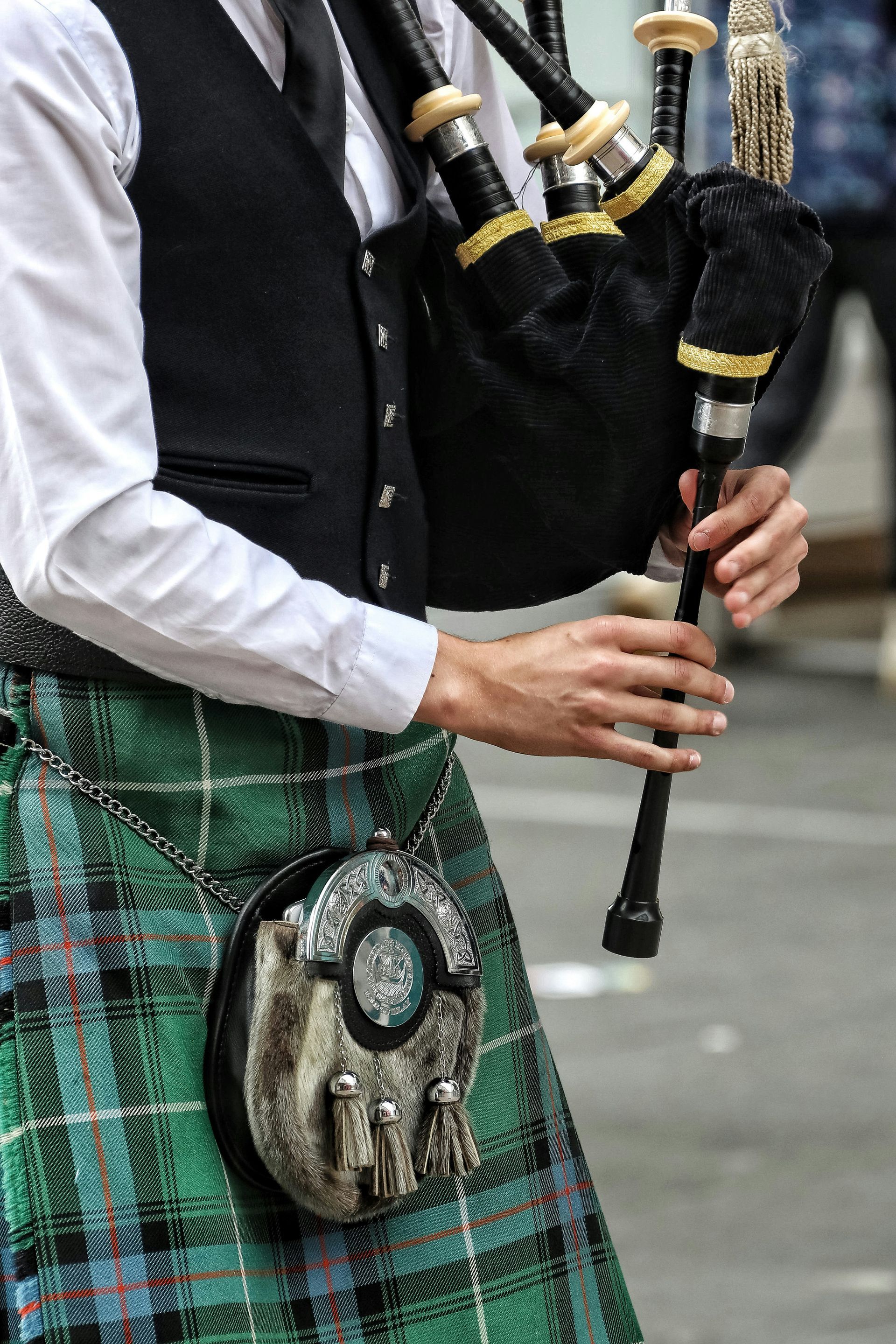 Person playing black bagpipes in traditional green tartan attire