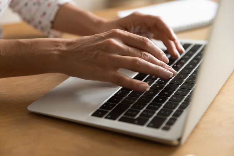 Hands typing on a silver laptop keyboard at a desk