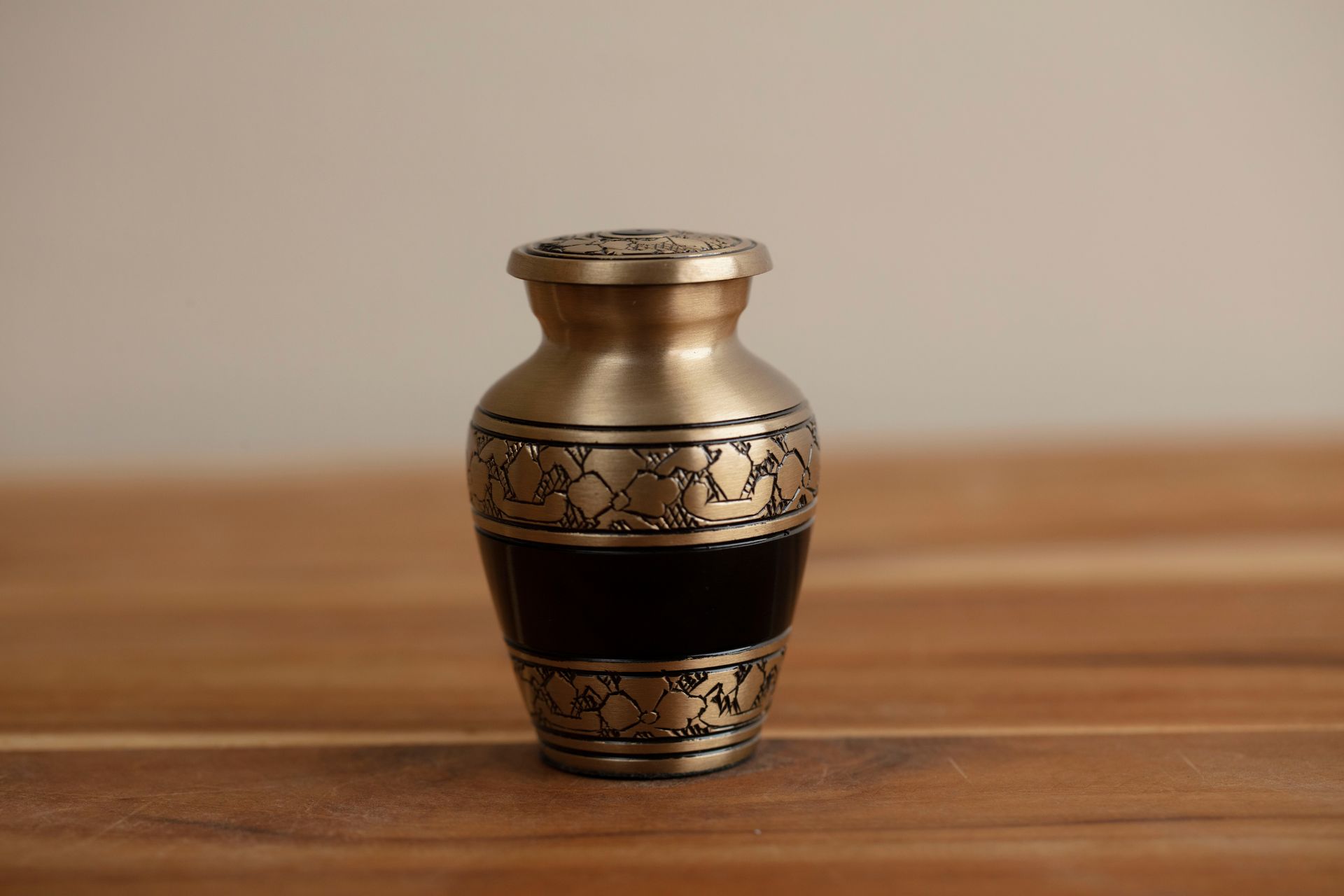 Small ornate brass vase with black inlay on a wooden surface